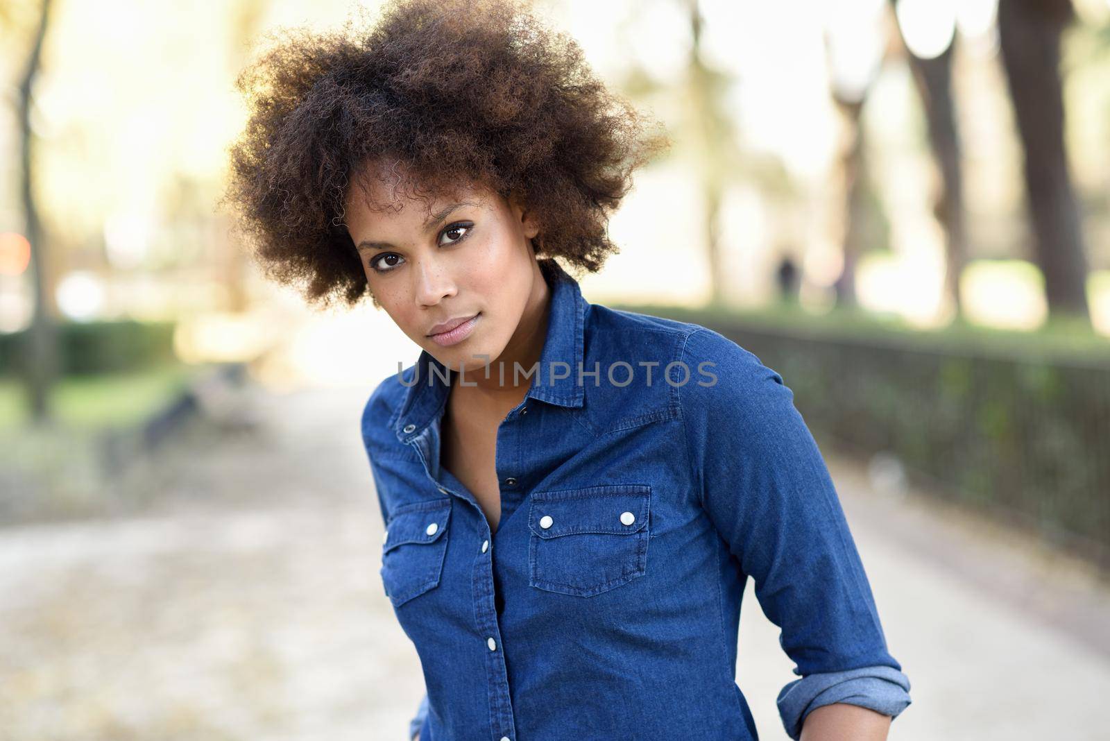 Young black woman with afro hairstyle standing in urban background. Mixed woman wearing blue shirt and shorts.