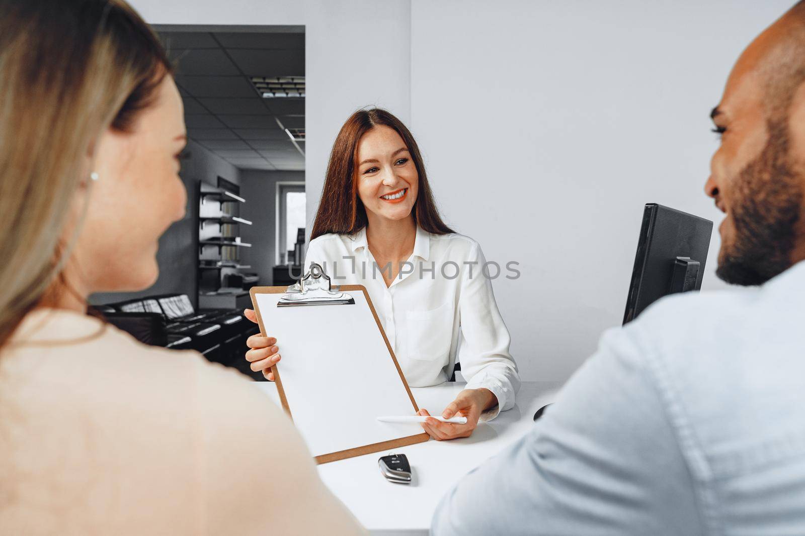 Young woman car seller showing contract to couple of car buyers by Fabrikasimf