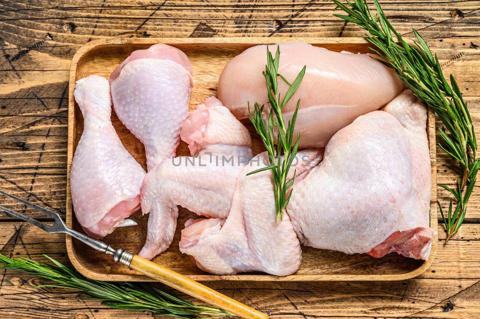 Fresh raw chicken meat, wings, breast, thigh and drumsticks on a wooden tray. Wooden background. Top view.