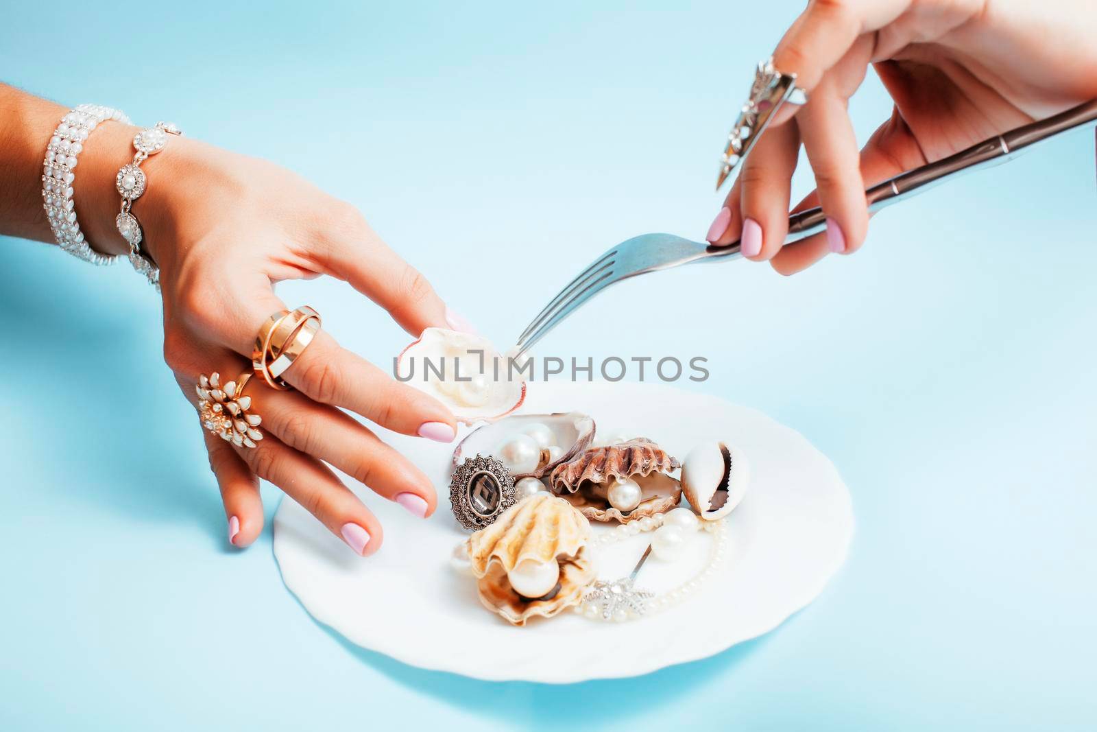 beautiful woman hands with pink manicure holding plate with pearls and sea shells, luxury jewelry concept close up