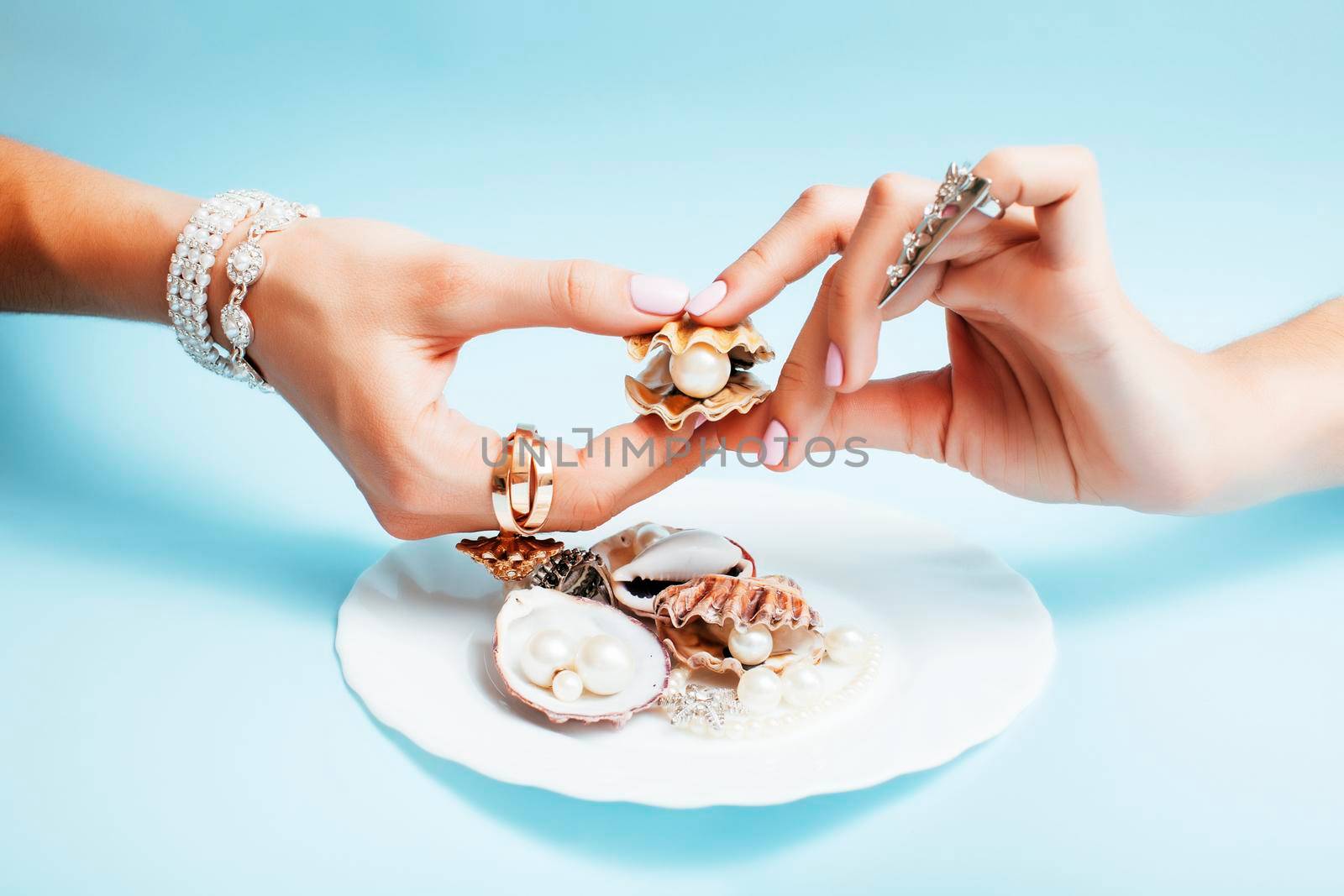 beautiful woman hands with pink manicure holding plate with pearls and sea shells, luxury jewelry concept by JordanJ