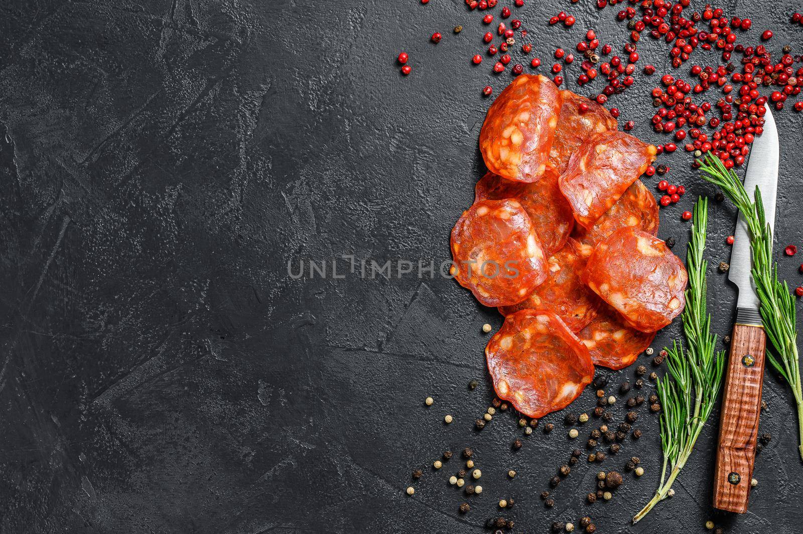 Chorizo sausage thin cut. Spanish salami with spices, paprika, pepper. Spicy food. Black background. Top view. Copy space.