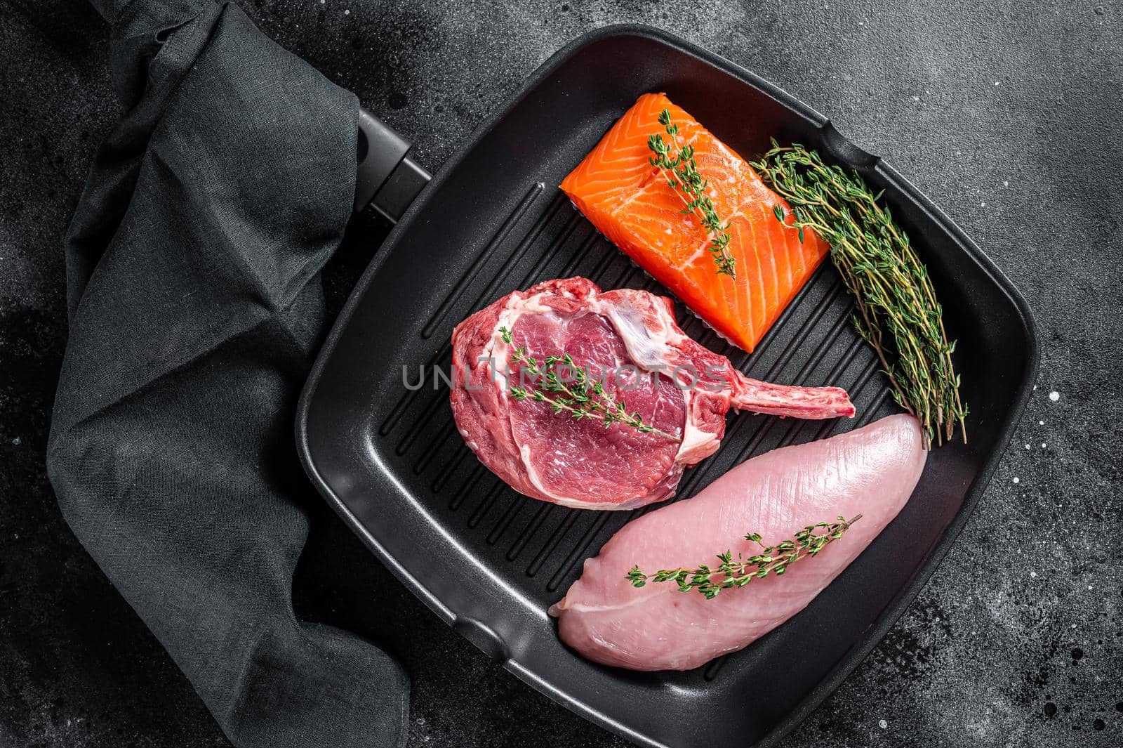 Cooking raw steaks. Fish salmon fillet, beef meat and turkey breast on a grill pan. Black background. Top view by Composter