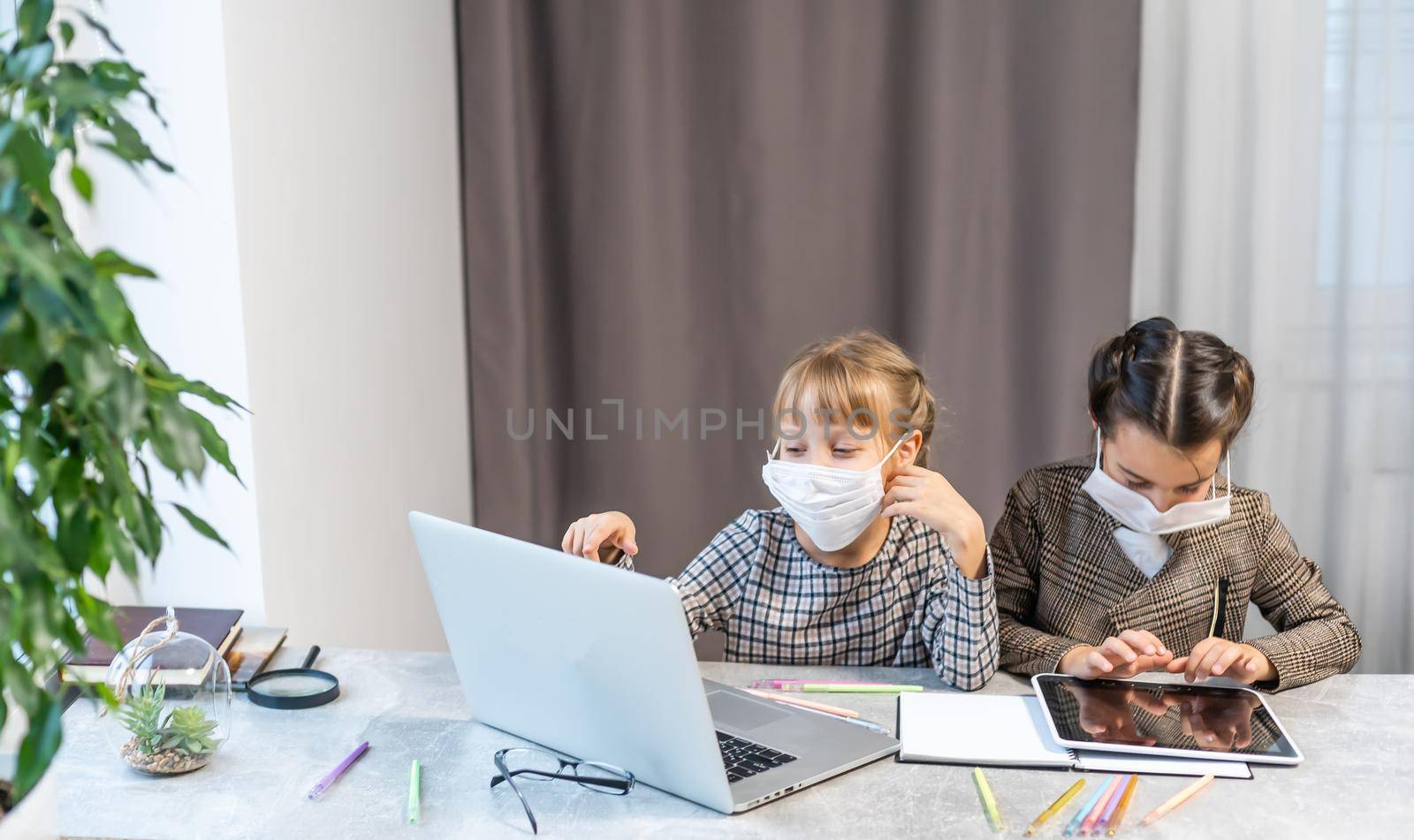 Distance Learning. School Girls At Laptop Wearing Mask Studying Online Sitting at the table at home by Andelov13