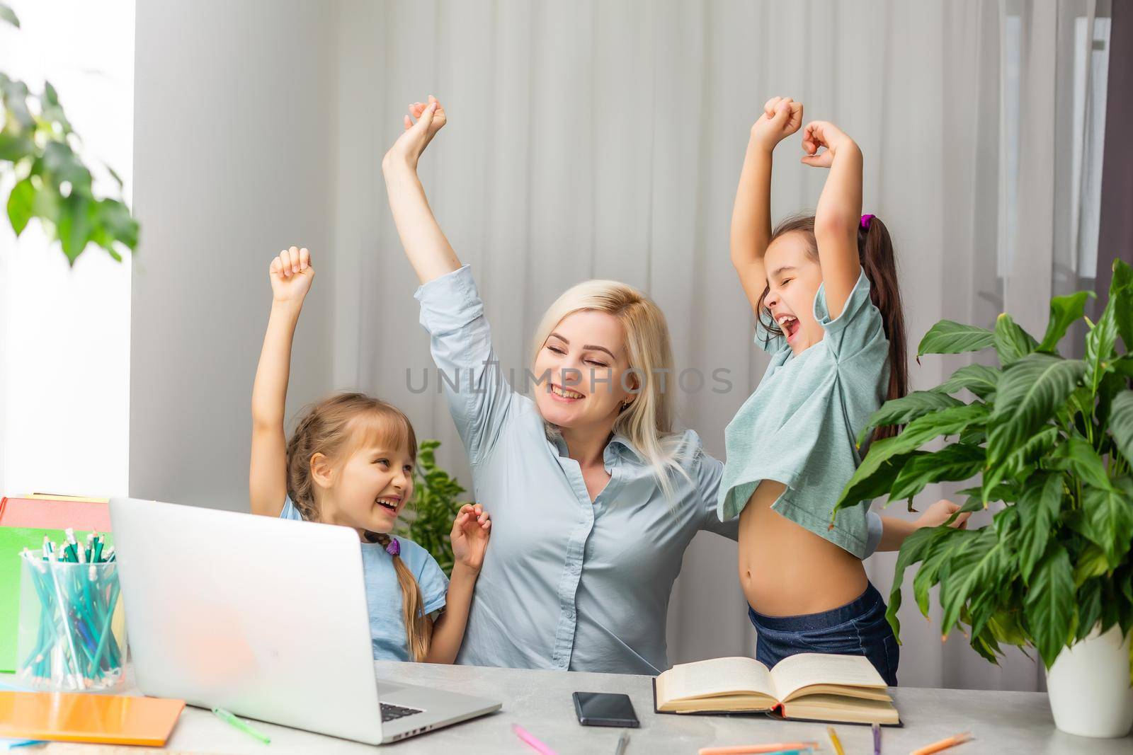 Happy mother and daughter are learning lessons in her mother's office at work. Woman teacher with girl study together sitting at the table near the computer monitor.