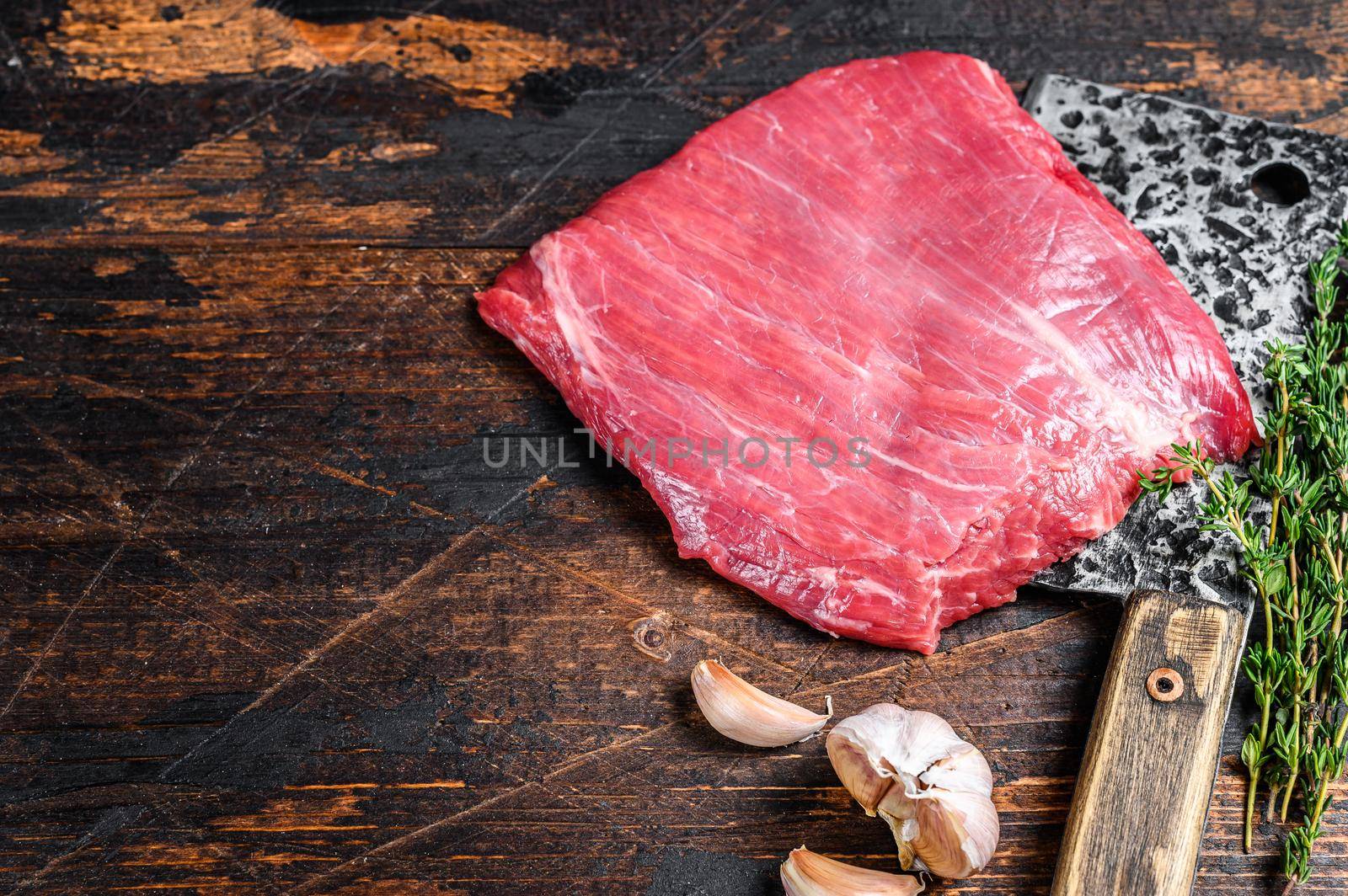 Raw flank beef marbled meat steak on a cleaver. Dark Wooden background. Top view. Copy space by Composter