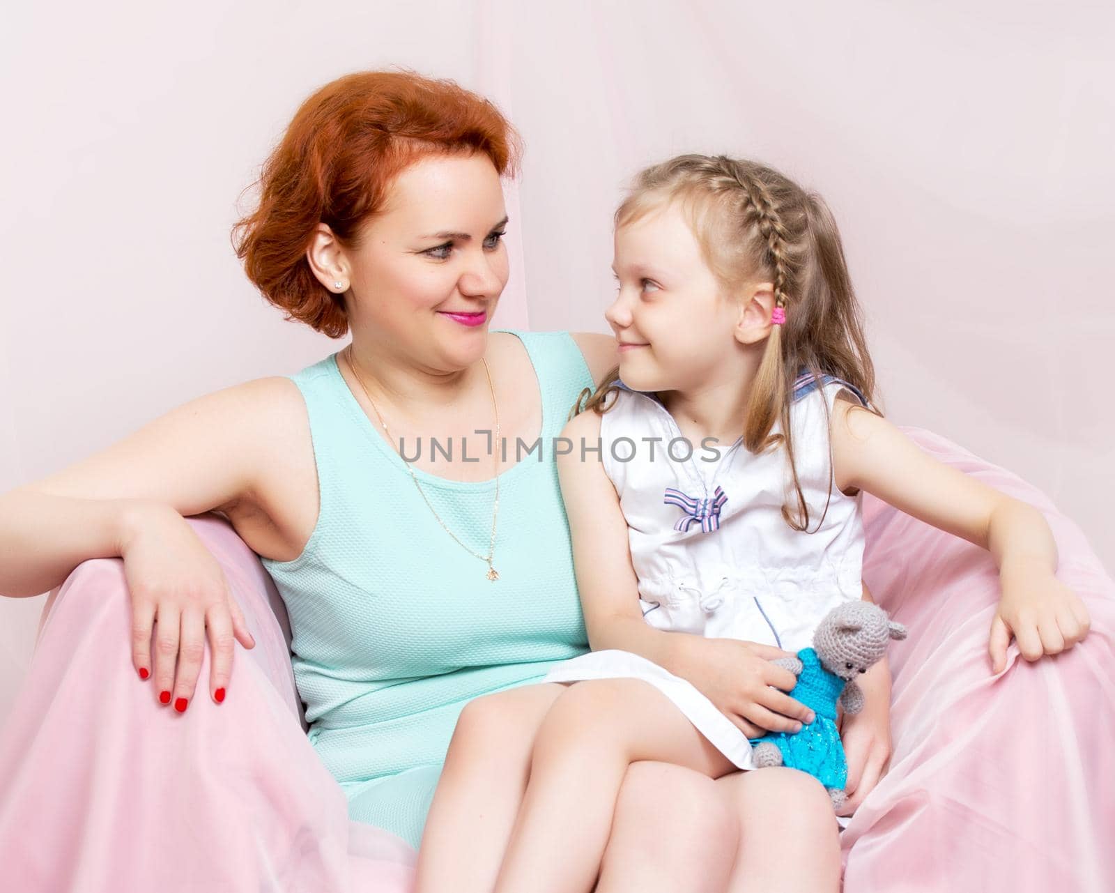 Mom and daughter are sitting on the couch. The concept of family happiness, parenthood, childhood. Isolated on white background.