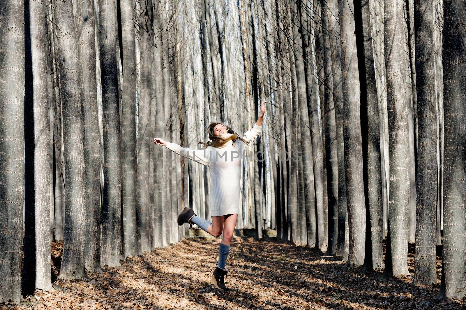 Beautiful blonde girl, dressed with beige dress, jumping into the wood