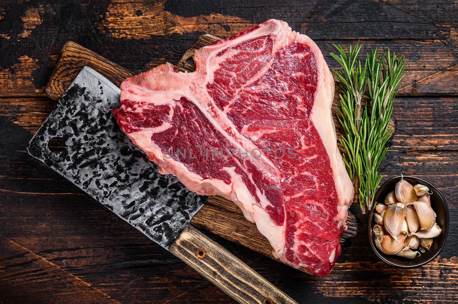 Italian Florentine T-bone beef meat Steak with herbs on a wooden cutting board. Dark wooden background. Top view by Composter