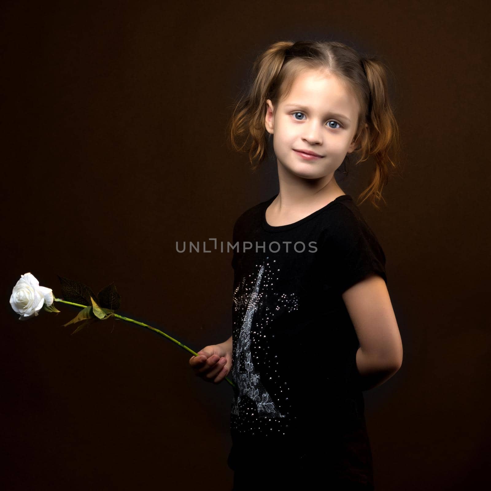 Beautiful little girl with a flower in her hand. The concept of style and fashion. On a black background.