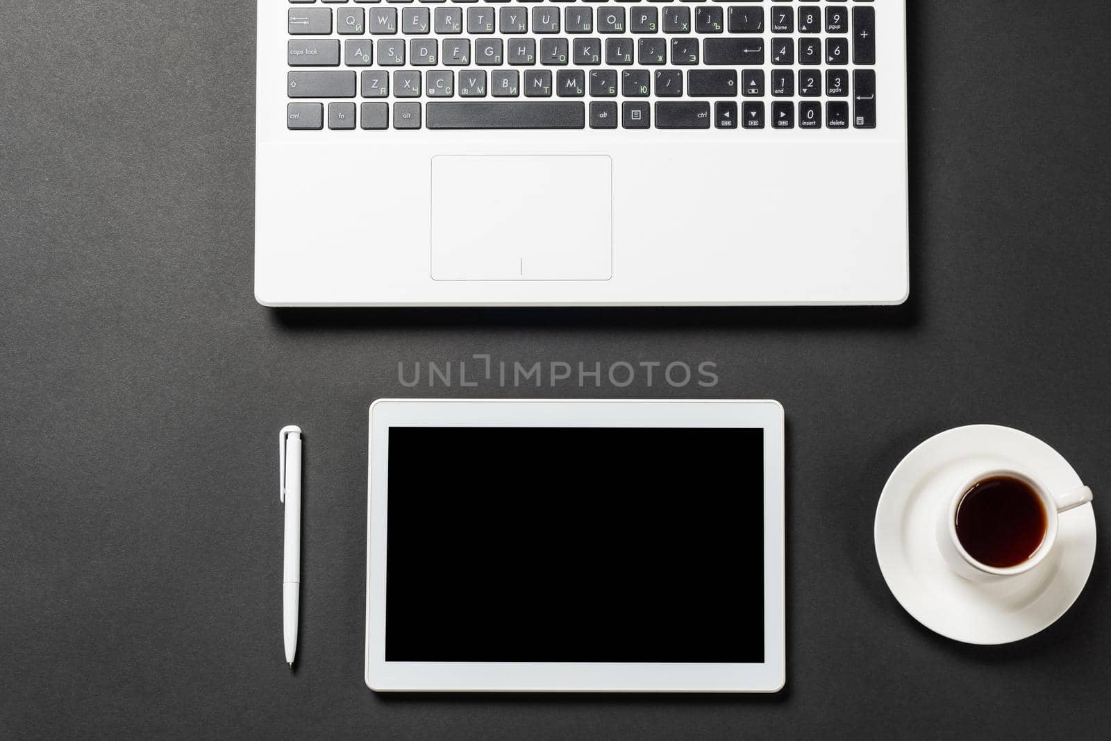 Still life of office workplace with laptop and cup of coffee. Flat lay black surface with tablet computer and pen. Top view modern coworking workspace and freelance. Digital technology and mobility.