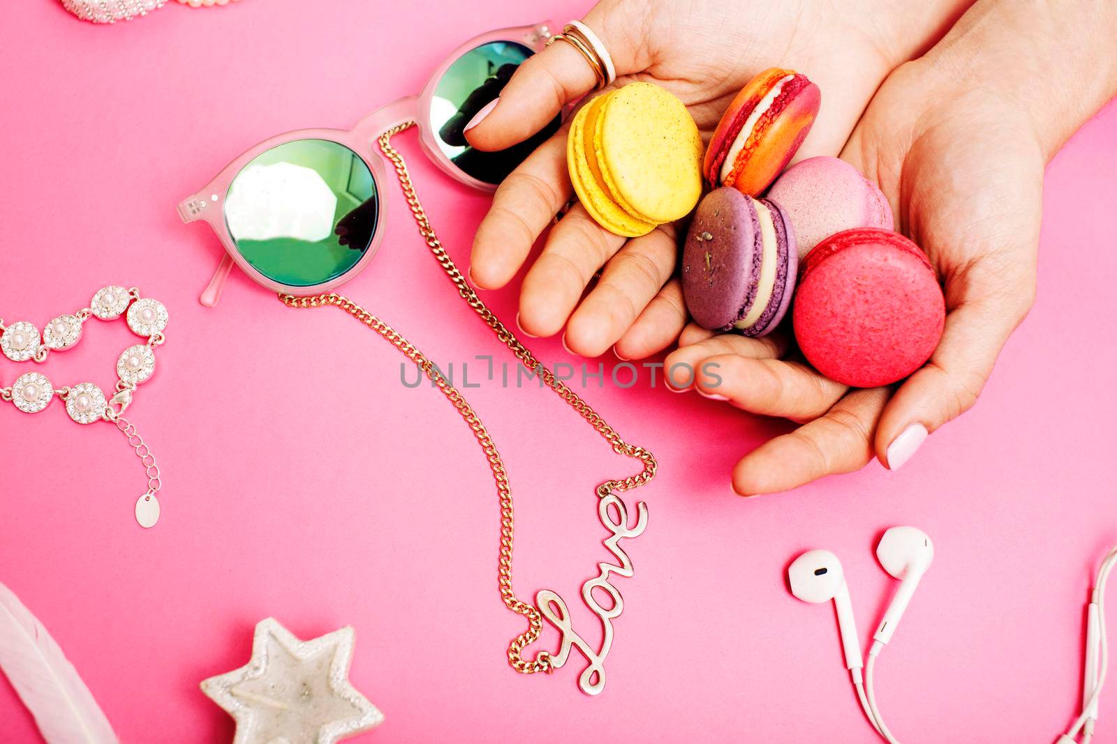 woman hands holding macaroons with lot of girl stuff on pink background, girls accessories concept close up