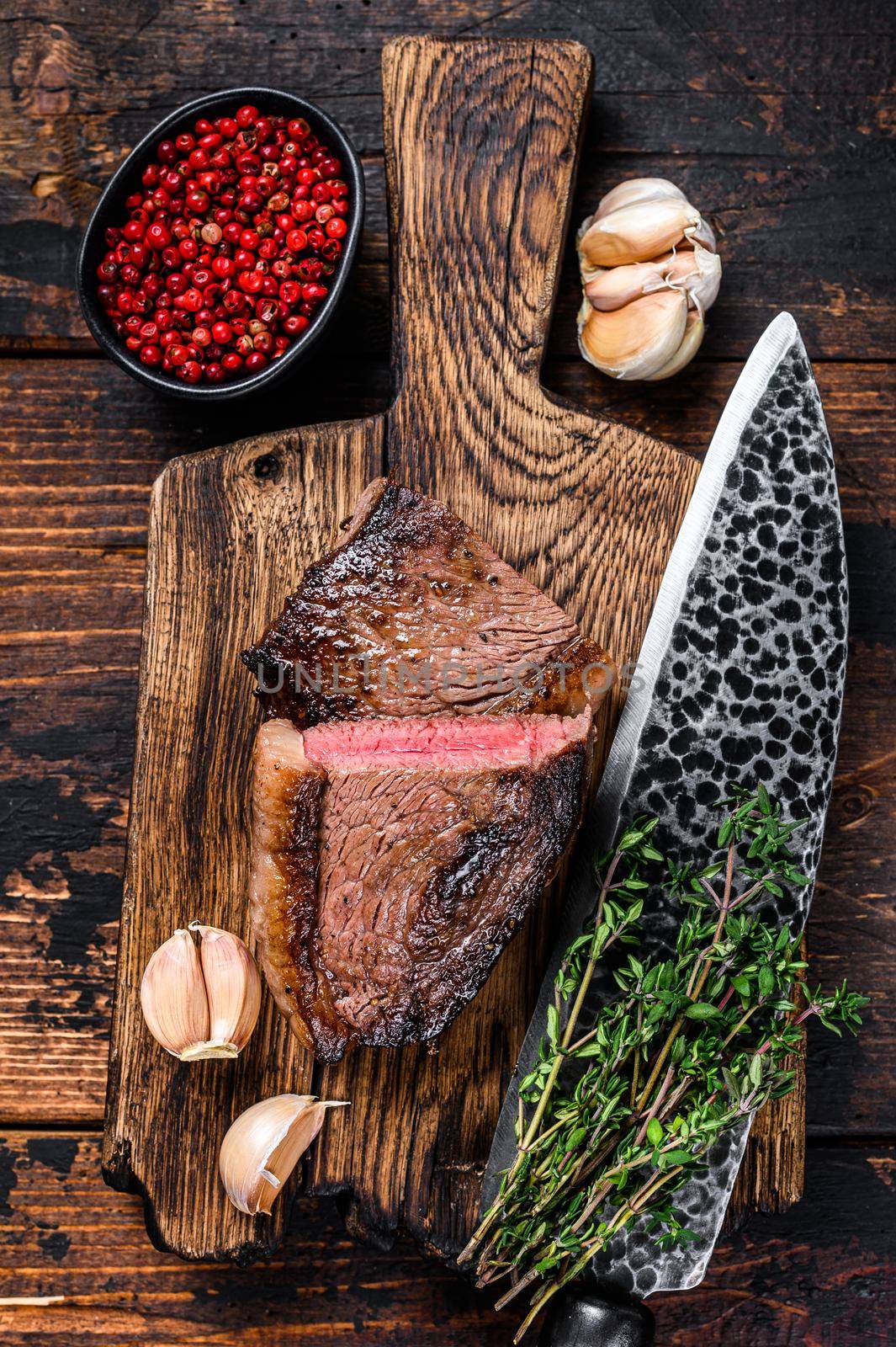 Cut fried rump cap or brazilian picanha beef meat steak on a wooden board. Dark wooden background. Top view by Composter