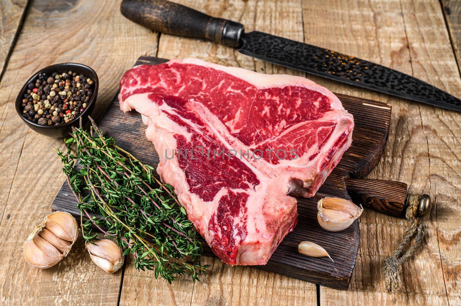 Raw Porterhouse or T-bone beef meat Steak with herbs on a wooden cutting board. wooden background. Top view by Composter