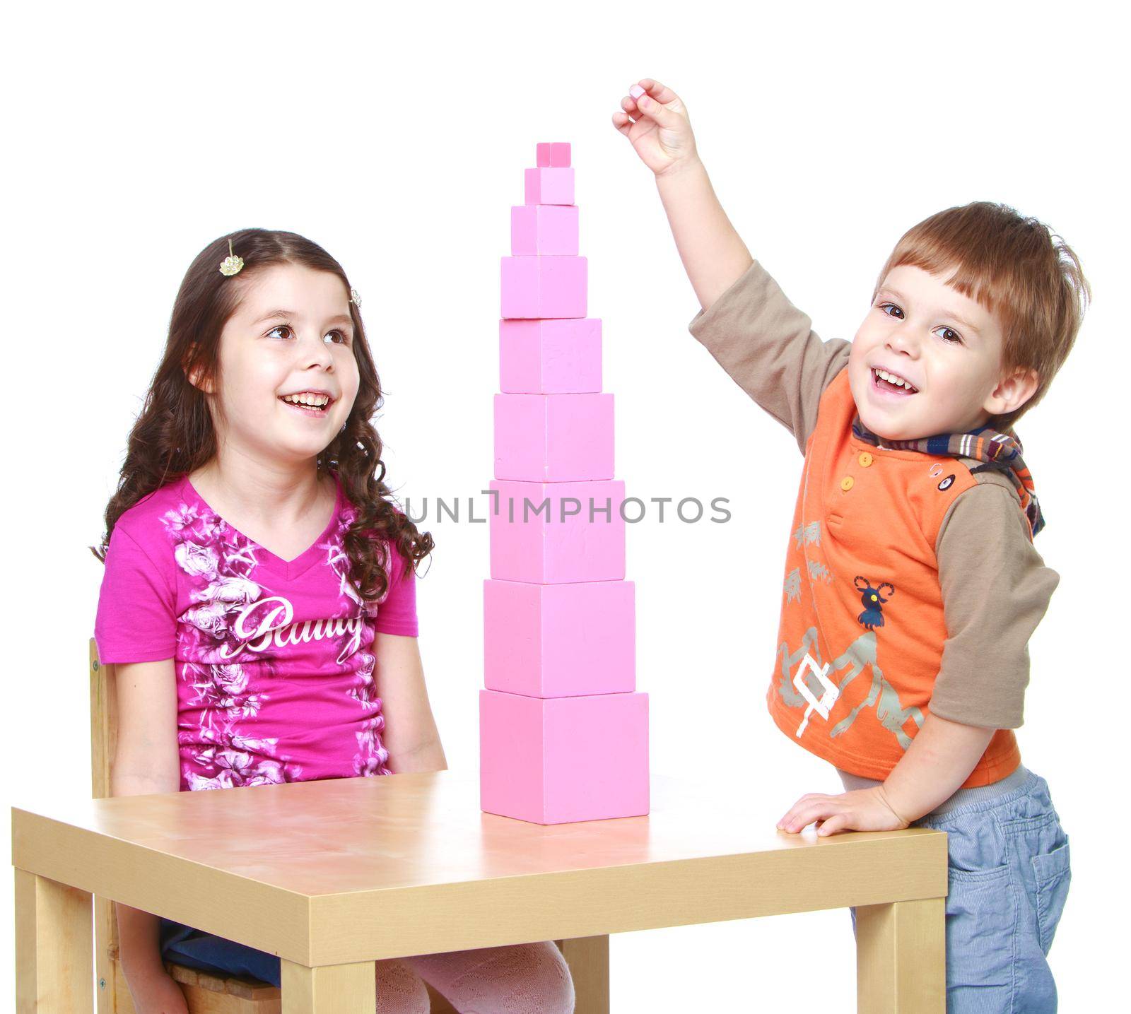 Smiling brother and sister playing together building pink tower, which stands on the table.Isolated on white background portrait.