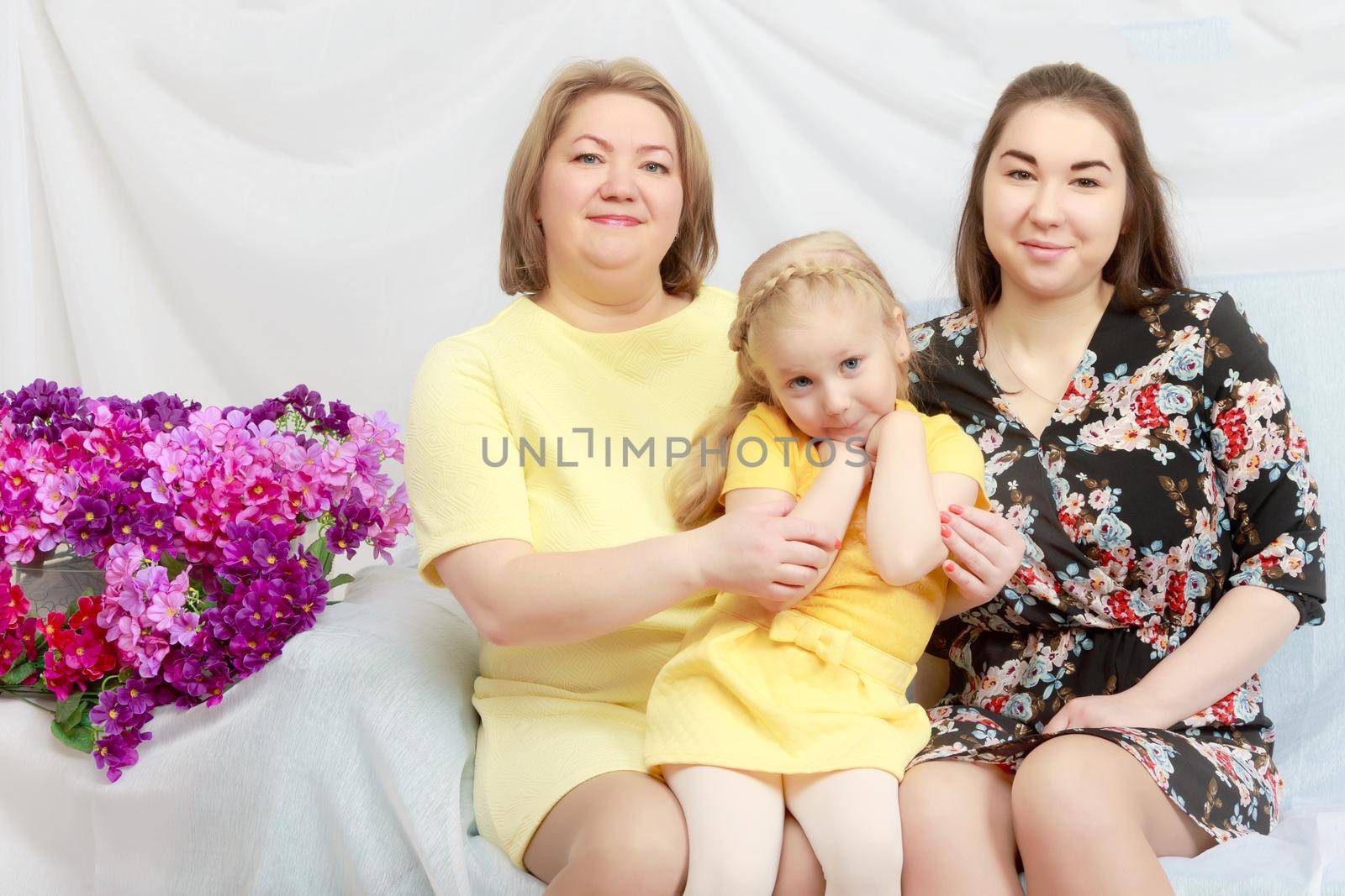 A happy mother hugs her beloved daughters. Senior and younger. Studio photo.Near a bouquet of flowers.