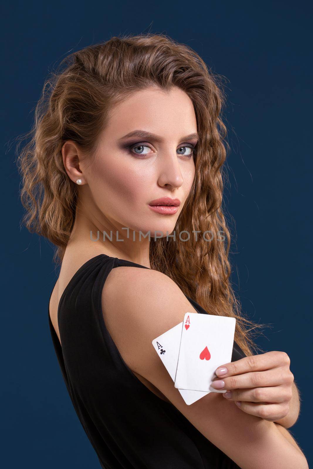 Beautiful woman in black dress holding two aces as a sign for poker game on dark blue background, gambling and casino