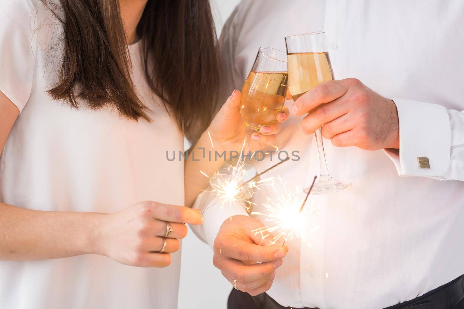 New year, holidays, date and valentines day concept - Loving couple holding sparklers light and glasses of champagne close-up over white background.