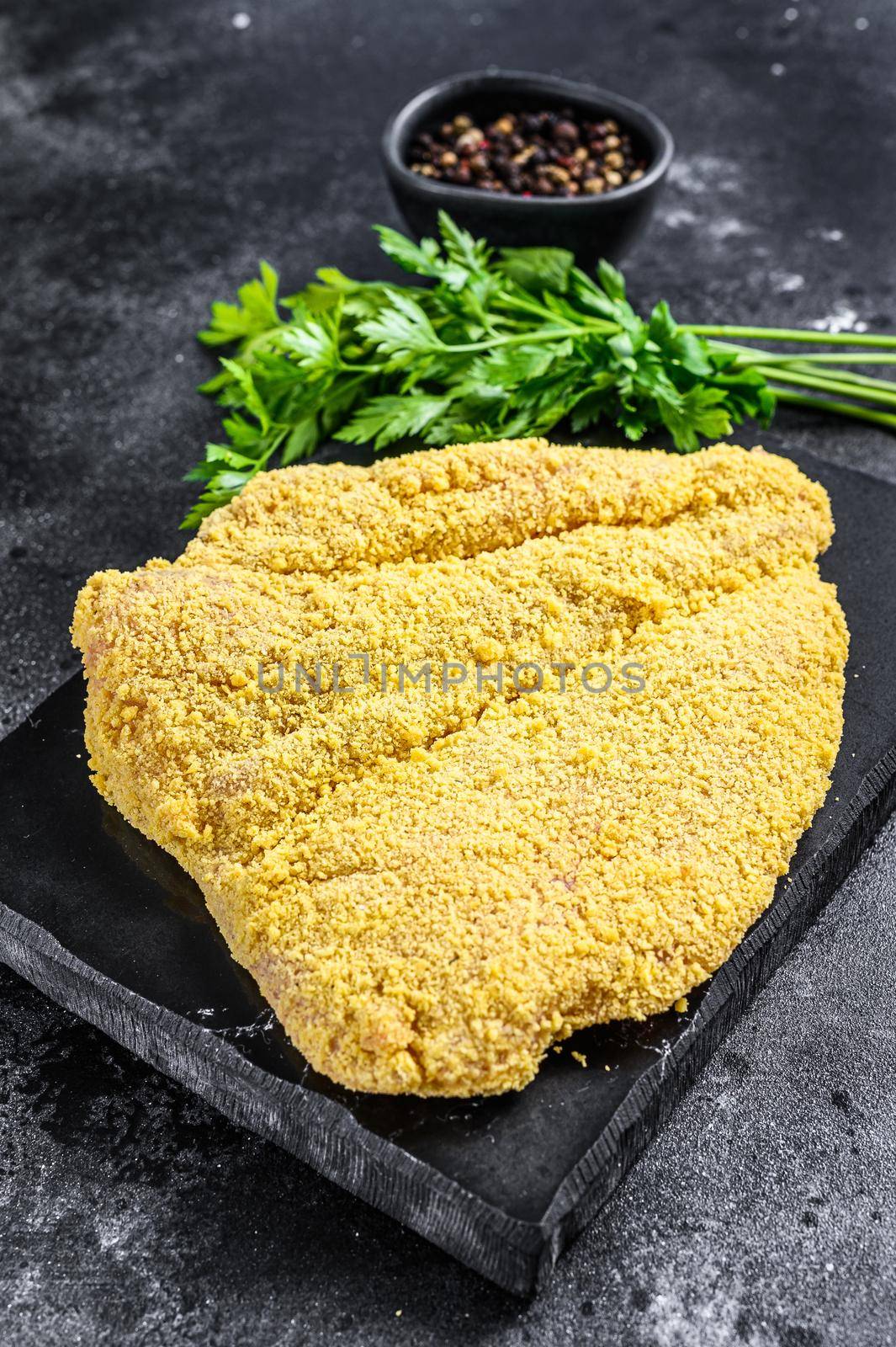 Raw large Viennese schnitzel on a cutting board. Black background. Top view.