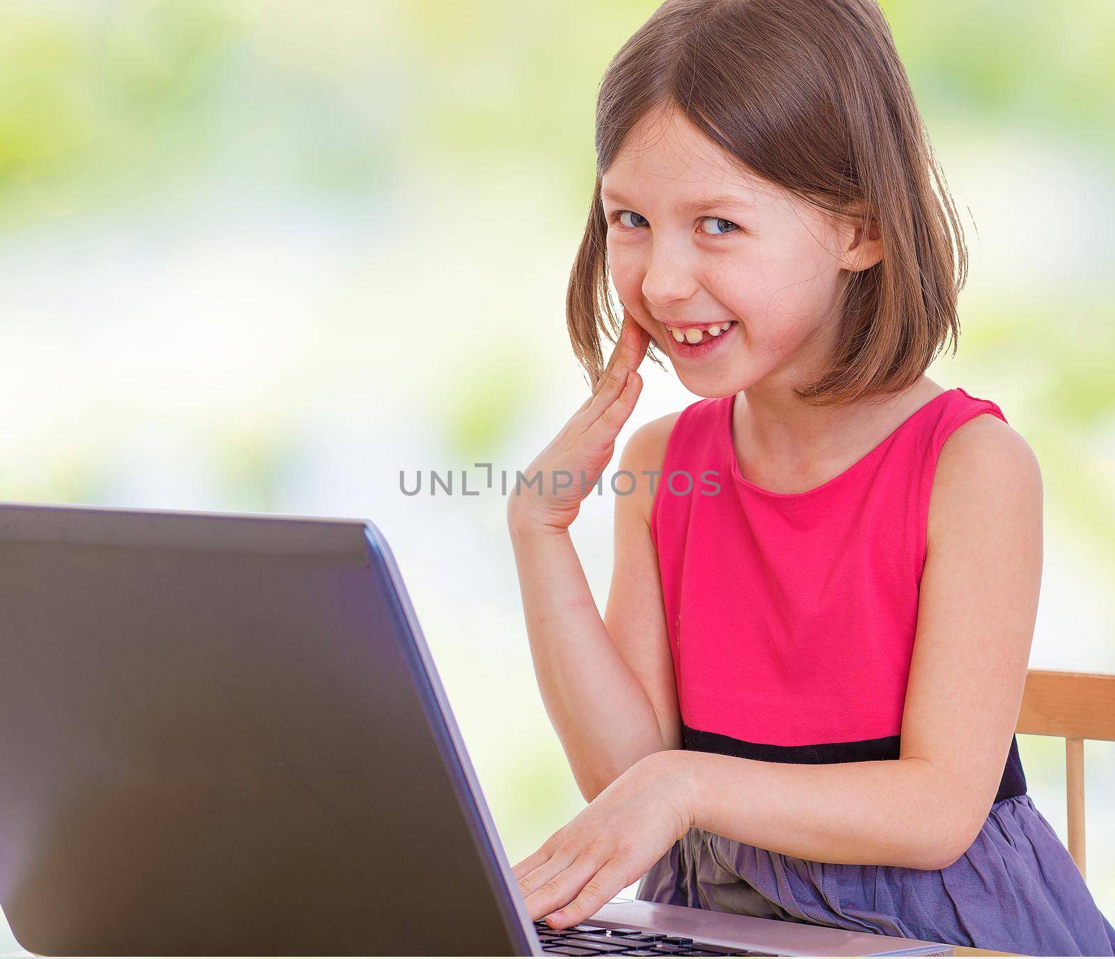 Little girl laughs looking at laptop screen.