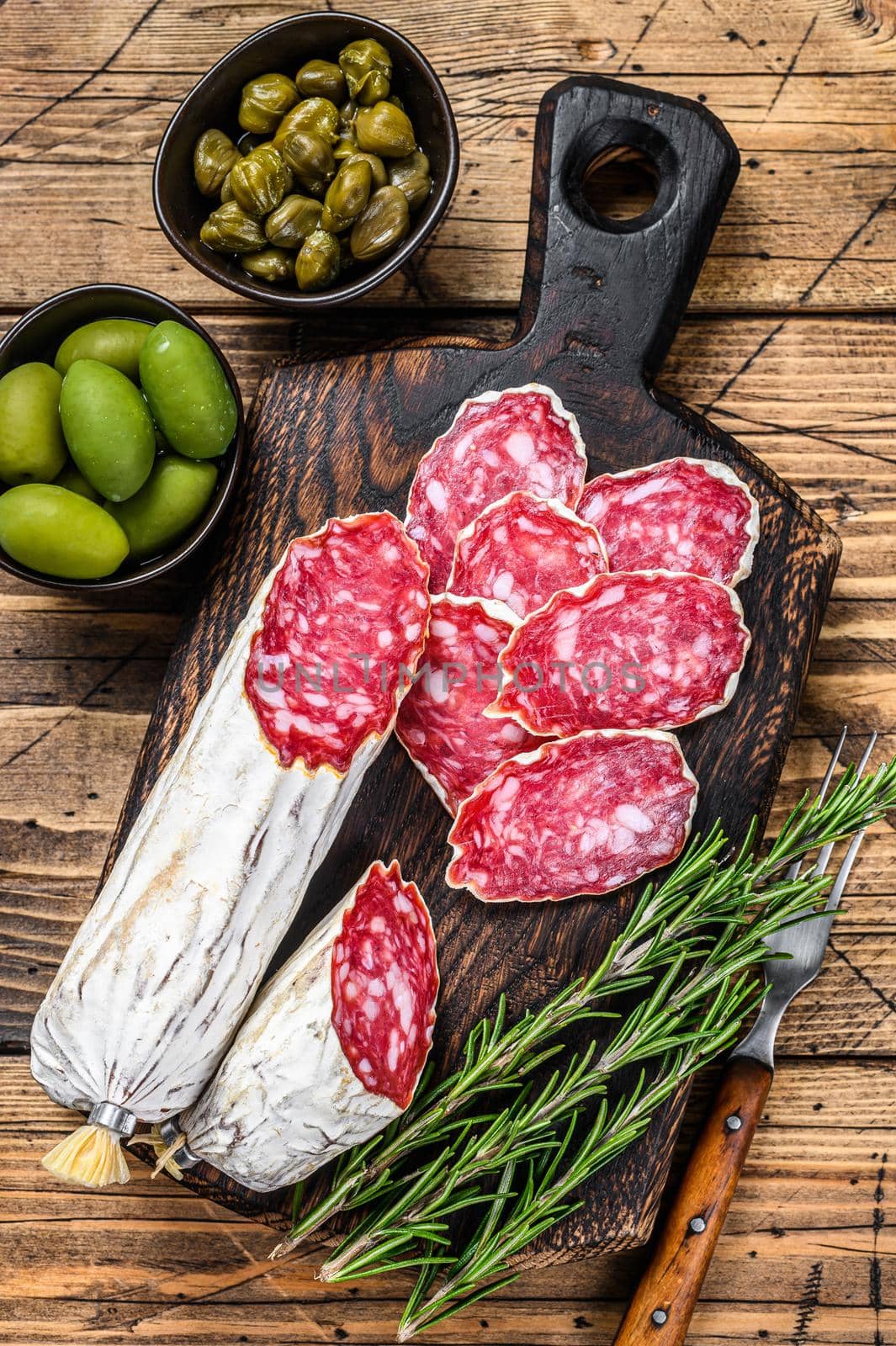 Thinly sliced salami salchichon on a wooden cutting board. wooden background. Top view.