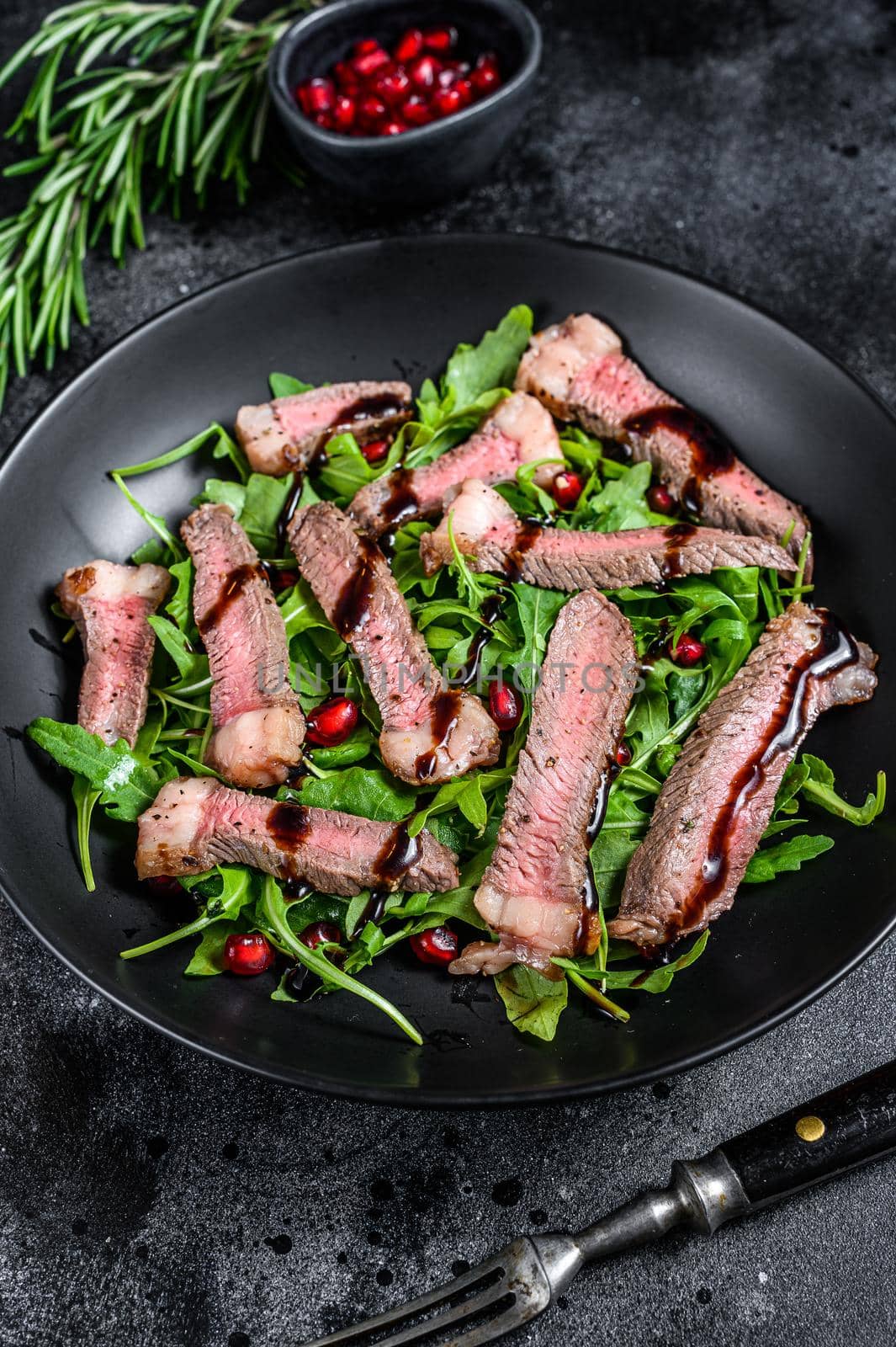 Grilled Beef Steak salad with arugula, pomegranate and greens vegetables. Black background. Top view by Composter