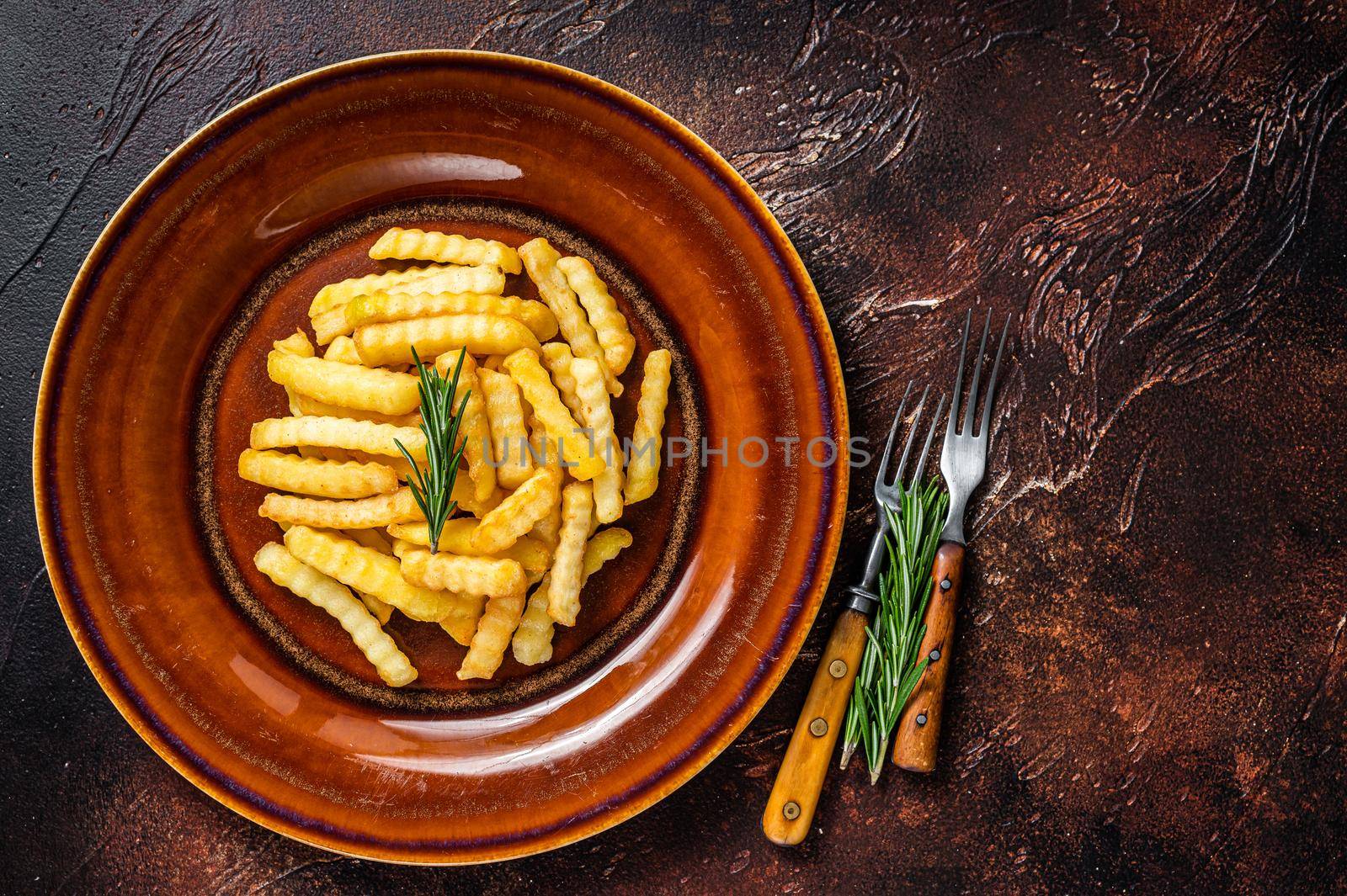 Fried Crinkle French fries potatoes or chips in a rustic plate. Dark background. Top view. Copy space by Composter