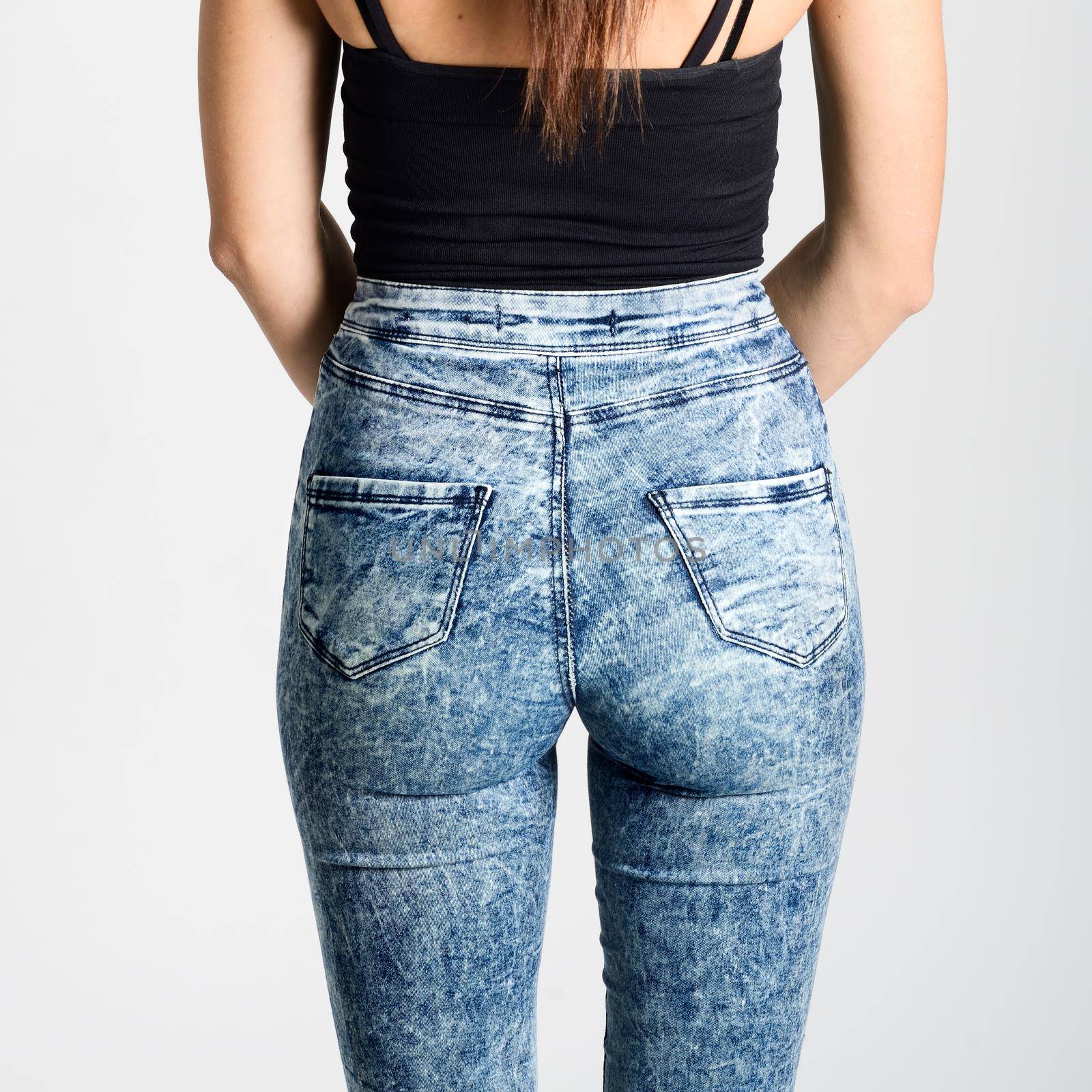 Back side of woman wearing high-waisted jeans. Studio shot. Girl with on white background