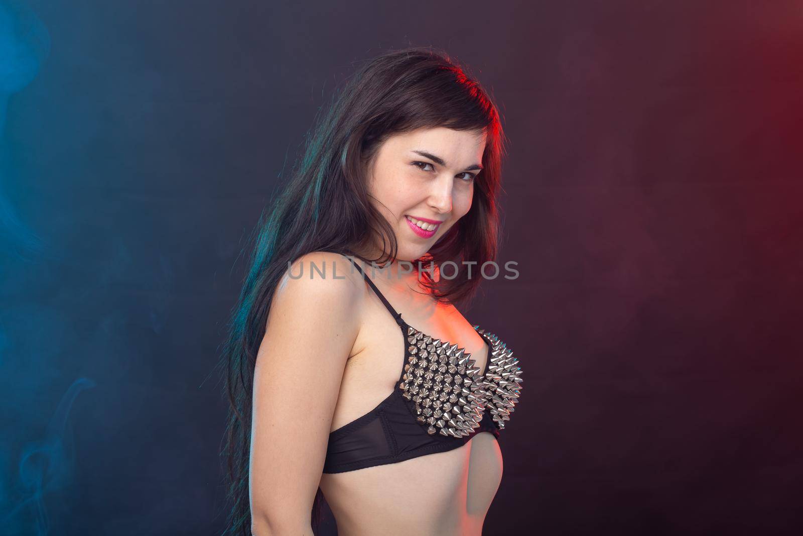 Beautiful young sexy brunette woman posing on a dark background in a riveted top on a dark background. The concept of grooming and attractiveness