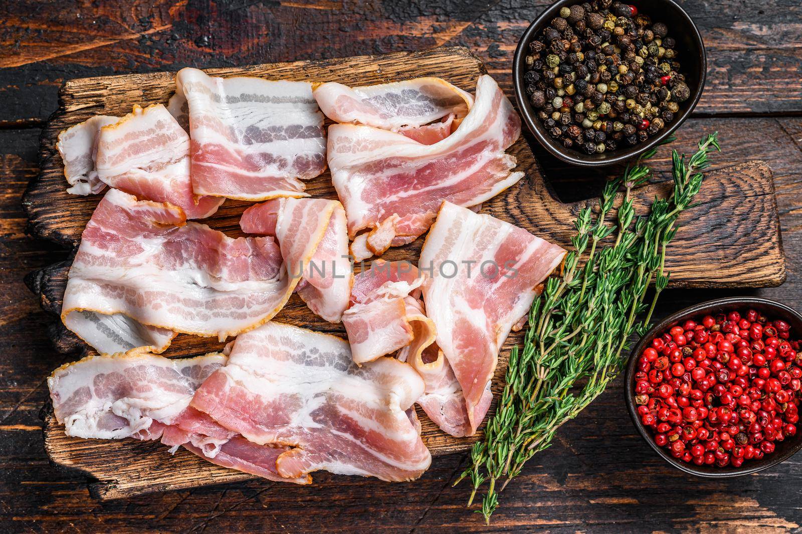 Raw pork bacon meat slices on a wooden cutting board. Dark wooden background. Top view.