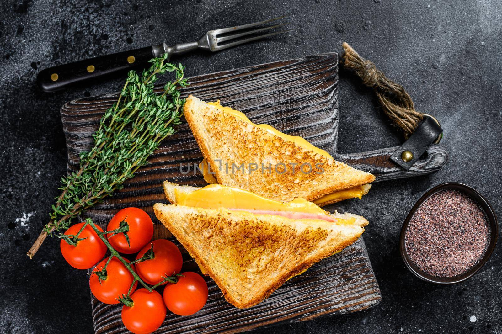 Grilled ham and cheese sandwich on a cutting board. Black background. Top view.