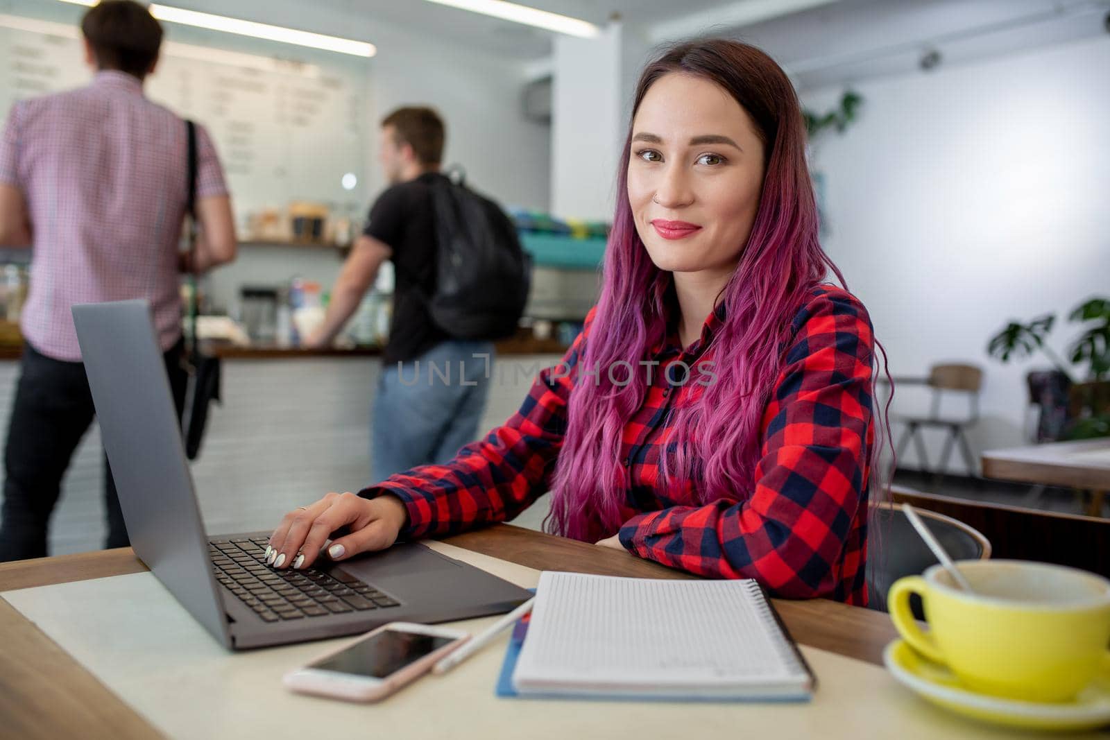 Young woman with pink hair with laptop computer sitting in cafe, intelligent female student working on net-book after her lectures in University