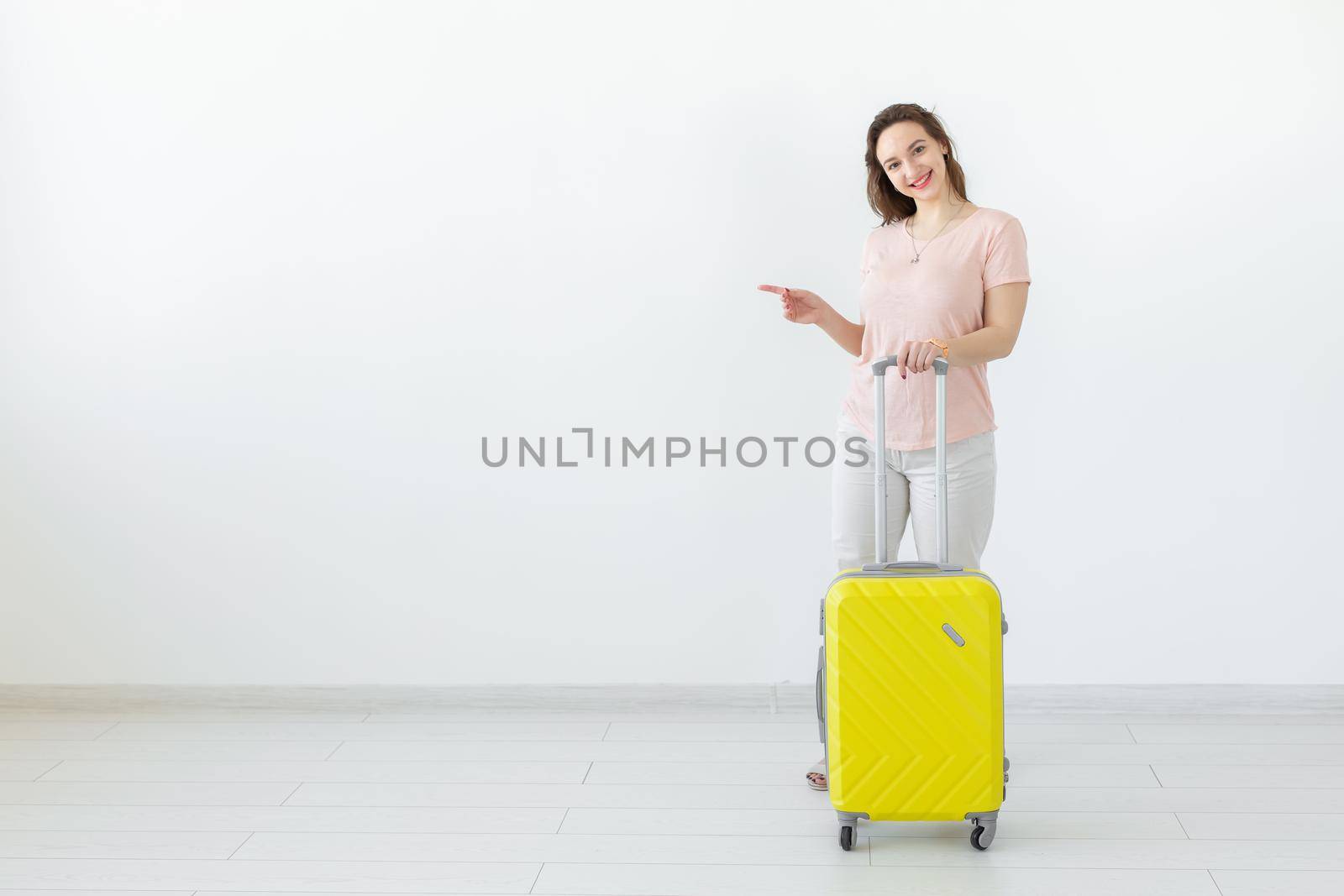 Trip, travel and holidays concept - woman with her yellow suitcase point on copy space.