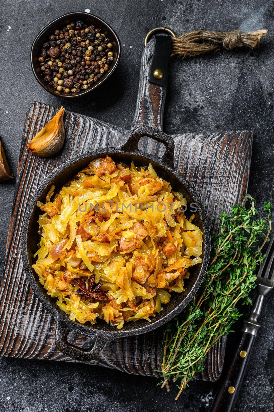 Stewed cabbage Bigos with mushrooms and sausages. Black background. Top view by Composter