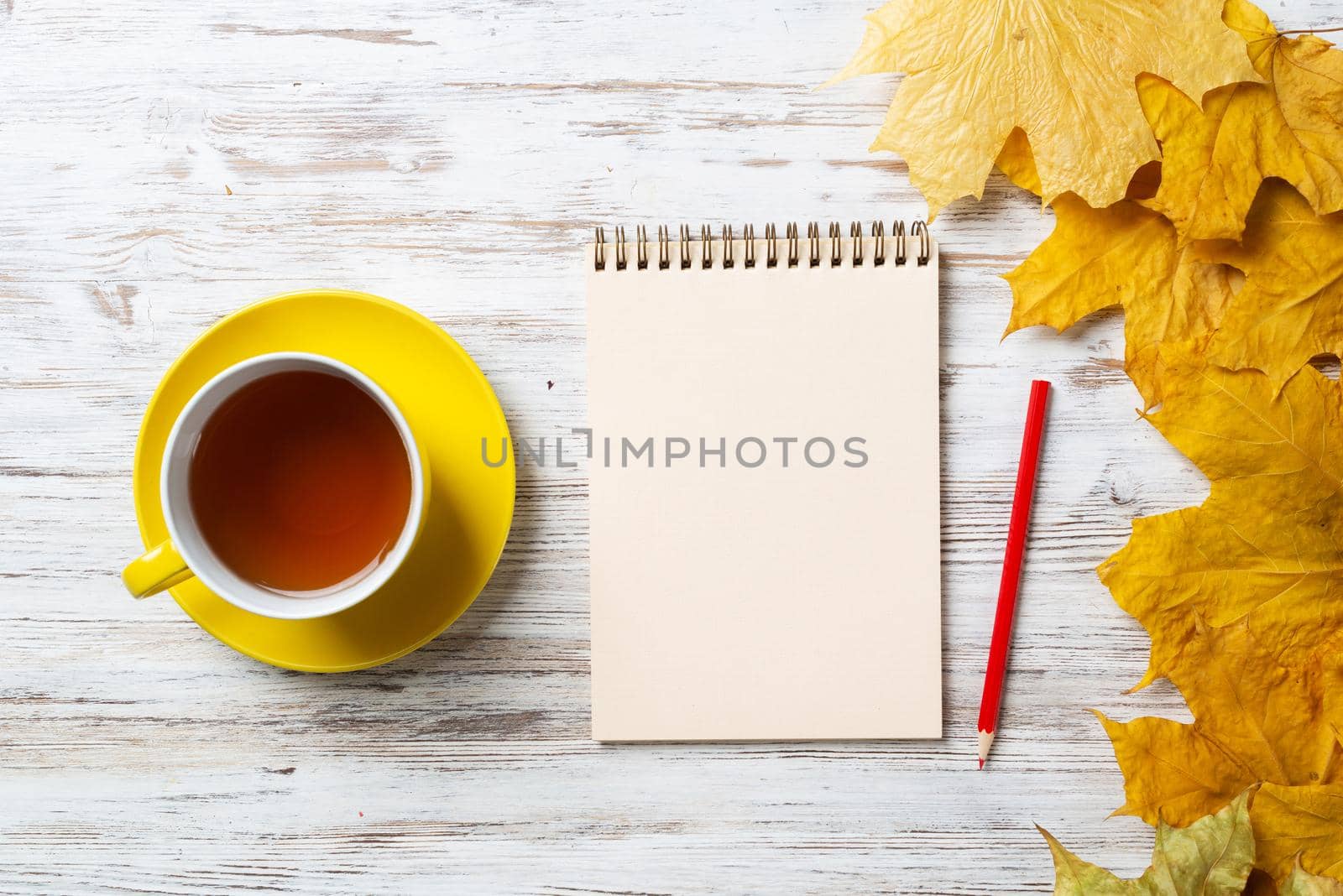 Flat lay autumn composition with cup of black tea and yellow autumn leaves. Time of tea break concept. Still life of hot drink and notepad with pen lies on vintage wooden desk with bright foliage.