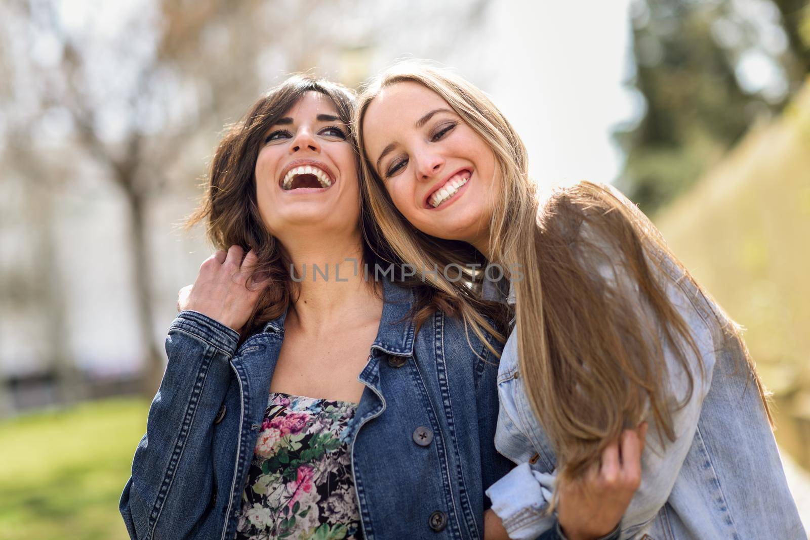 Two happy young women friends hugging in the street. by javiindy