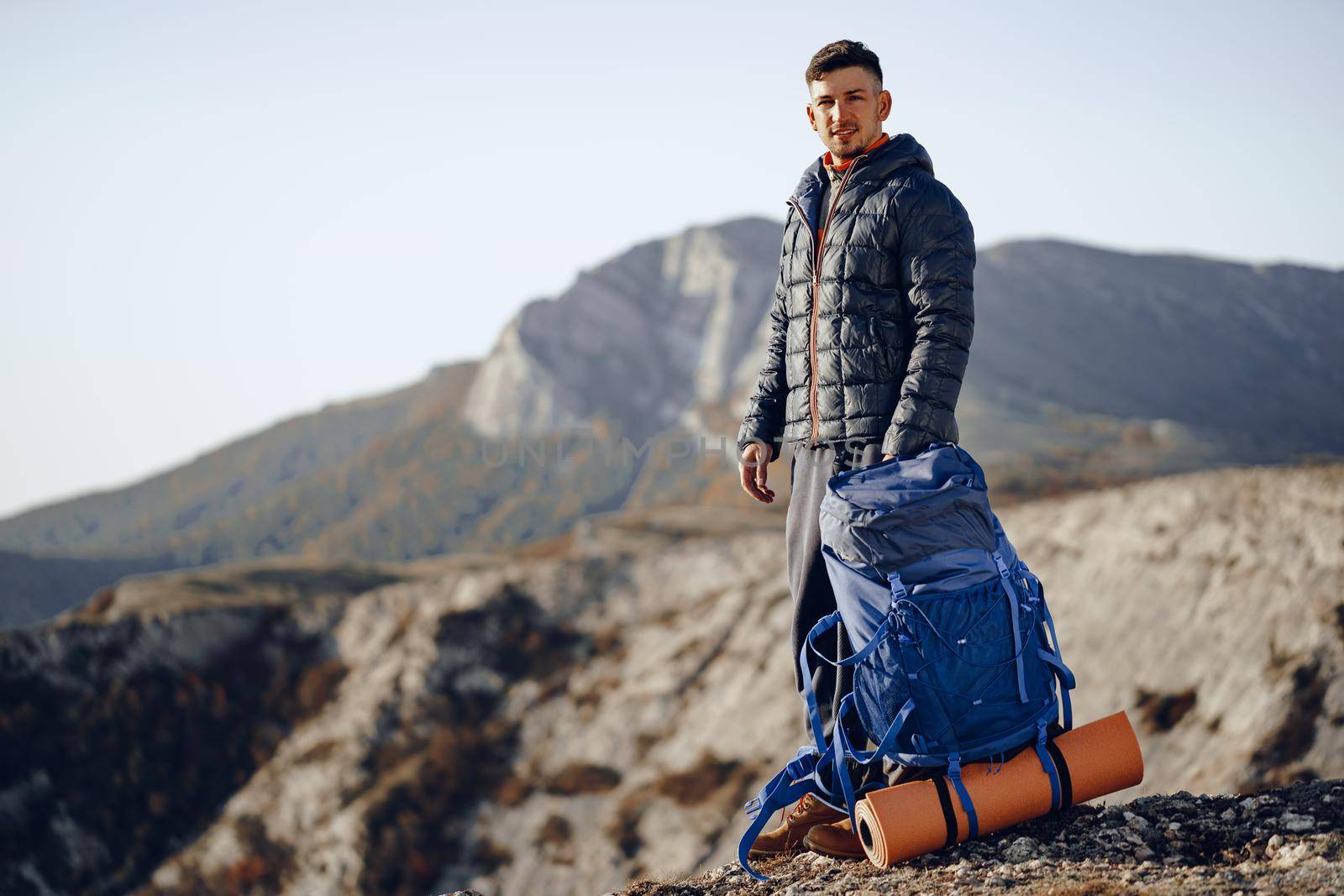 Male backpacker or hiker in hiking equipment standing at the top of the mountain