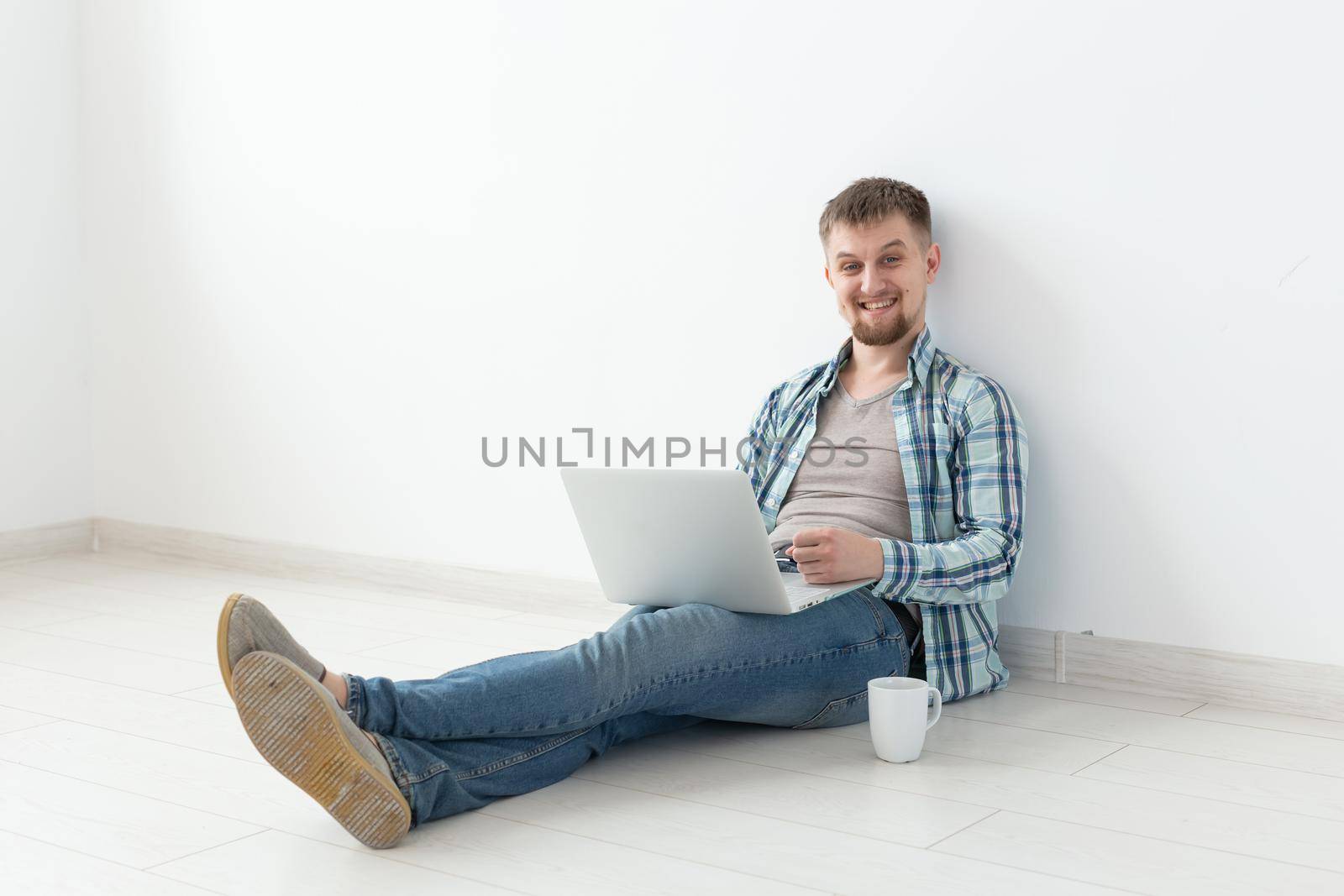 Positive young man in casual clothes and glasses surfing the Internet using Wi-Fi and a laptop in search of rental housing. Housewarming and apartment search concept
