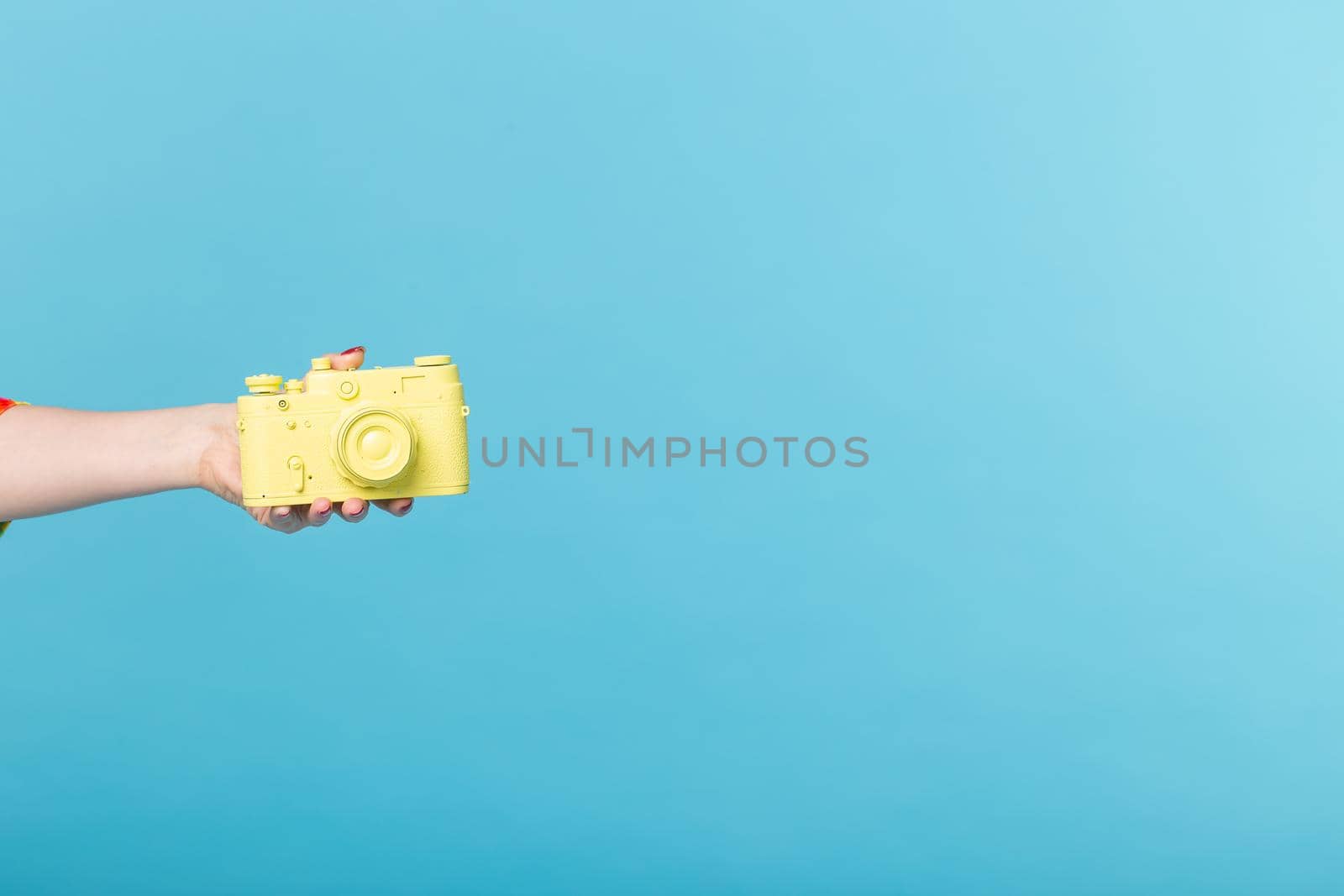 Photographing and vintage concept - female hand with yellow retro camera on pink background with copy space