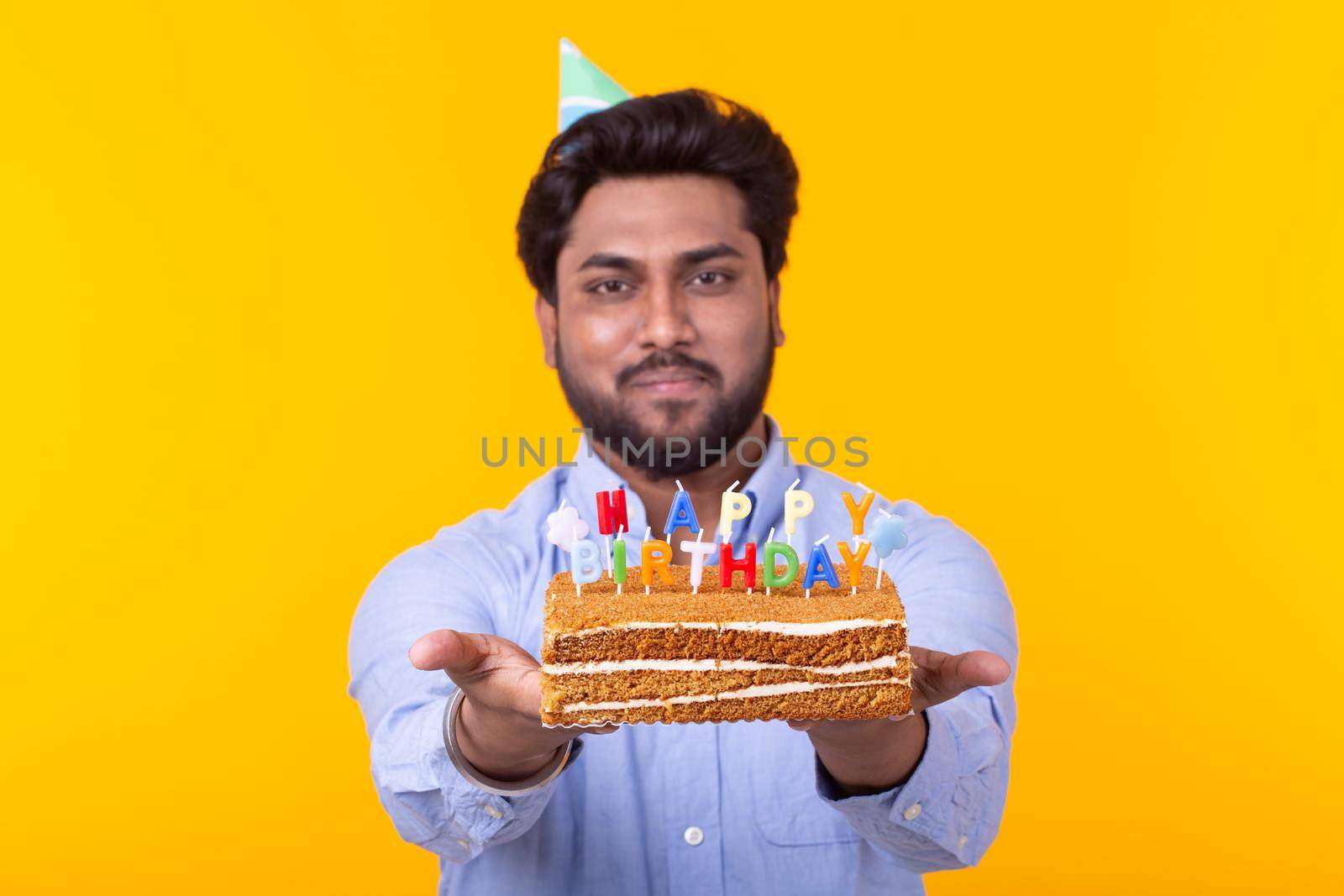 Funny positive guy in glasses holds in his hands a cake with the inscription happy birthday posing on a yellow background. Concept of holidays and anniversaries. Advertising space