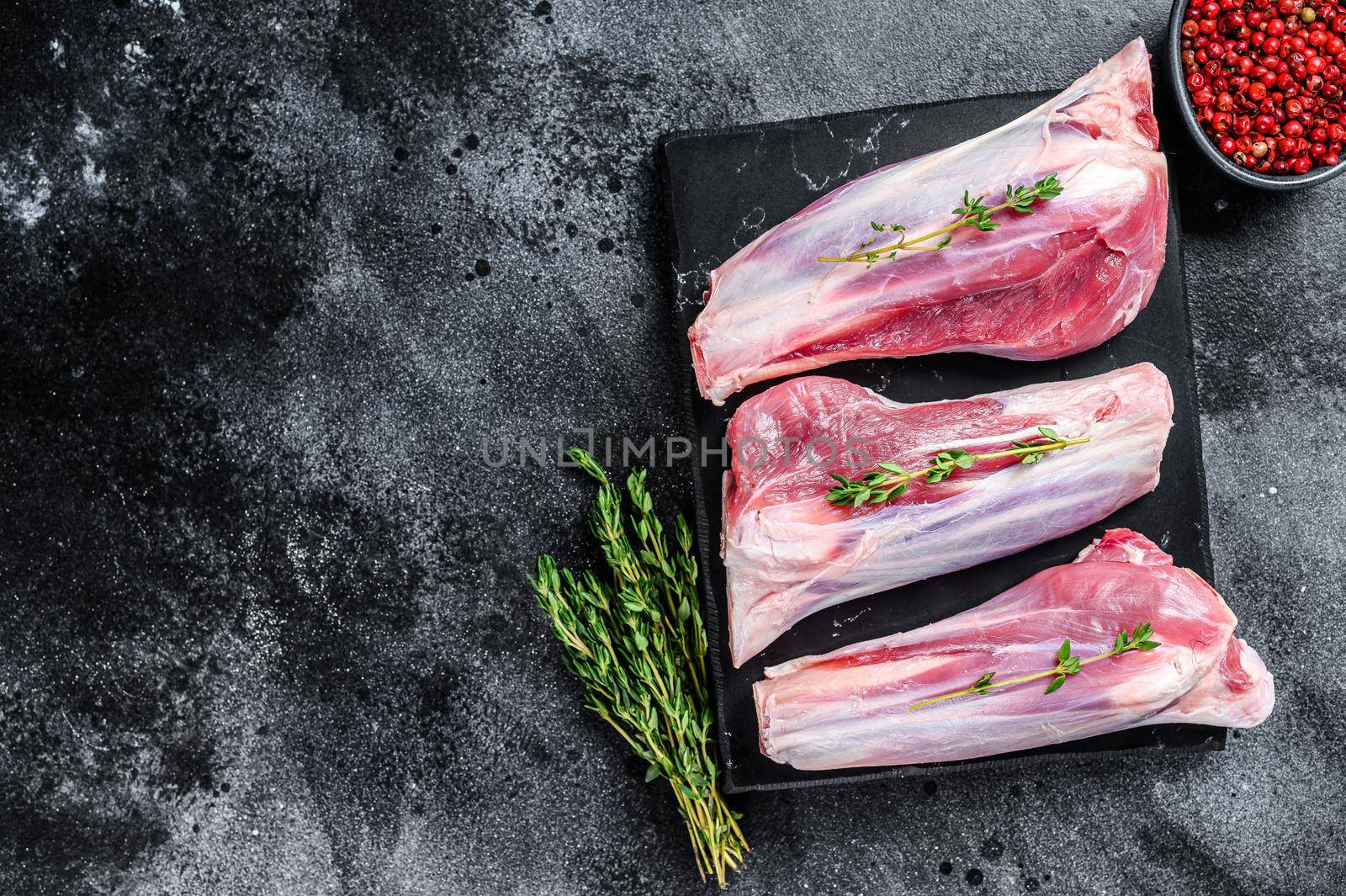 Raw lamb shanks meat on a marble board. Black background. Top view. Copy space.