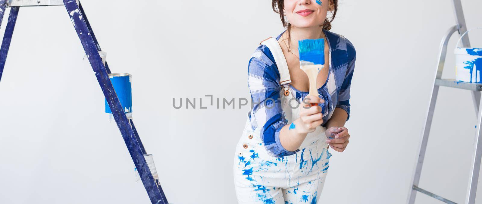 Repair, renovation and people concept - young woman painting the wall and looks like very happy, she with colorful cheek.