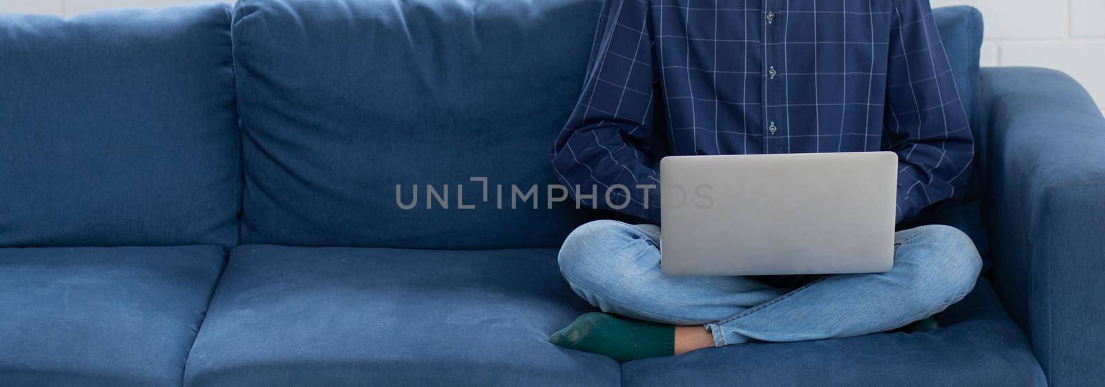 Young asian businessman smile and work from home with laptop computer online to internet on sofa in living room, freelance man using notebook on couch with comfort, new normal, lifestyle concept.