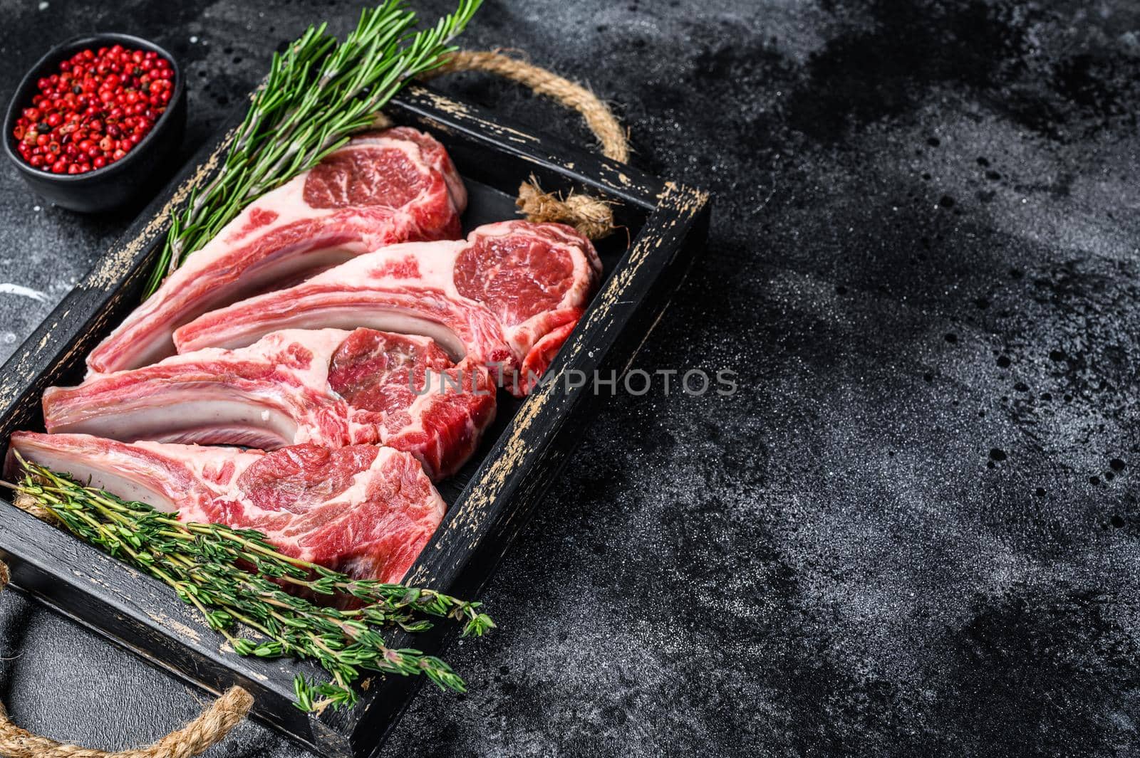 Raw lamb meat chops steaks in a wooden tray. Black background. Top view. Copy space by Composter