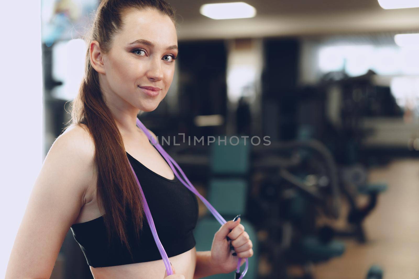 Portrait of a pretty fit girl with jumping rope standing in a gym