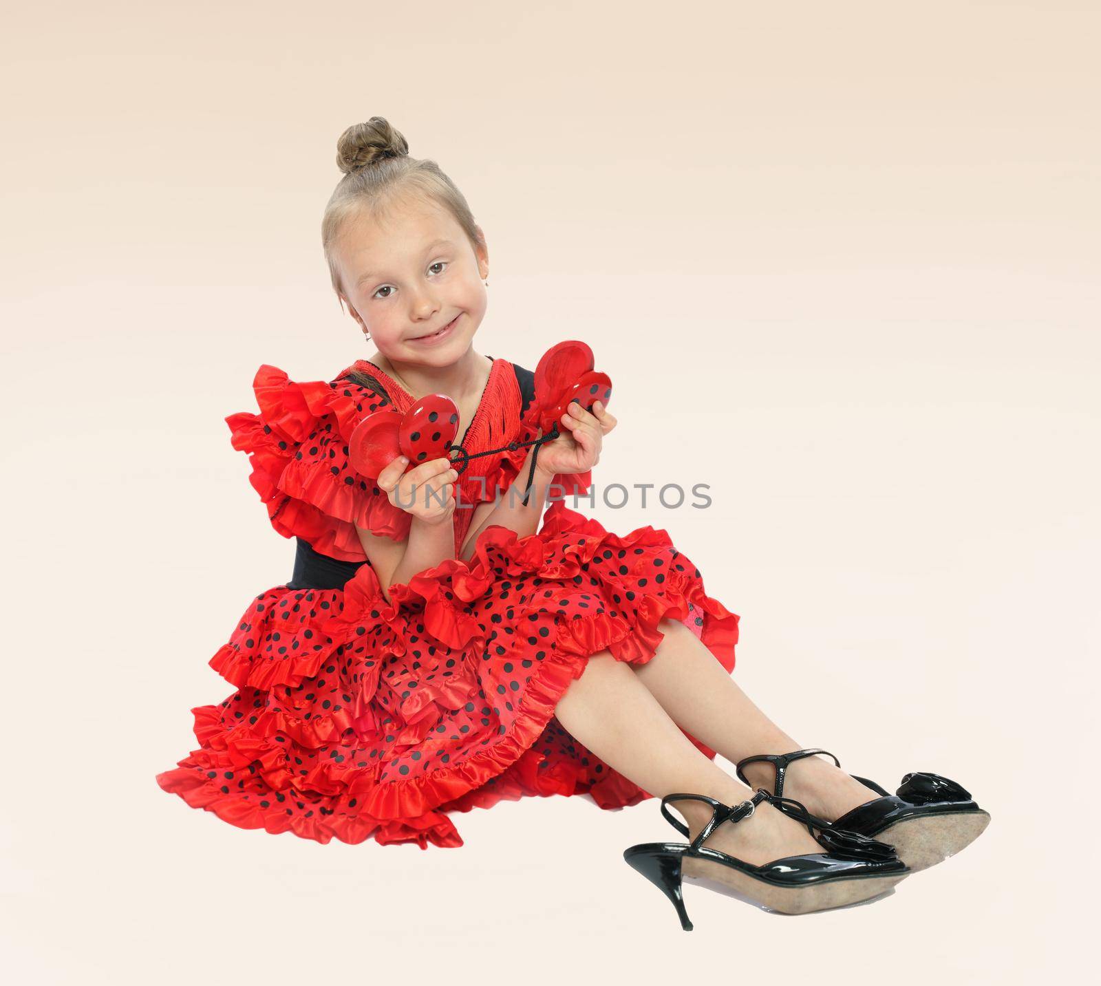 little girl in a bright red dress sitting on the floor in shoes on a high heel.the concept of fashion.