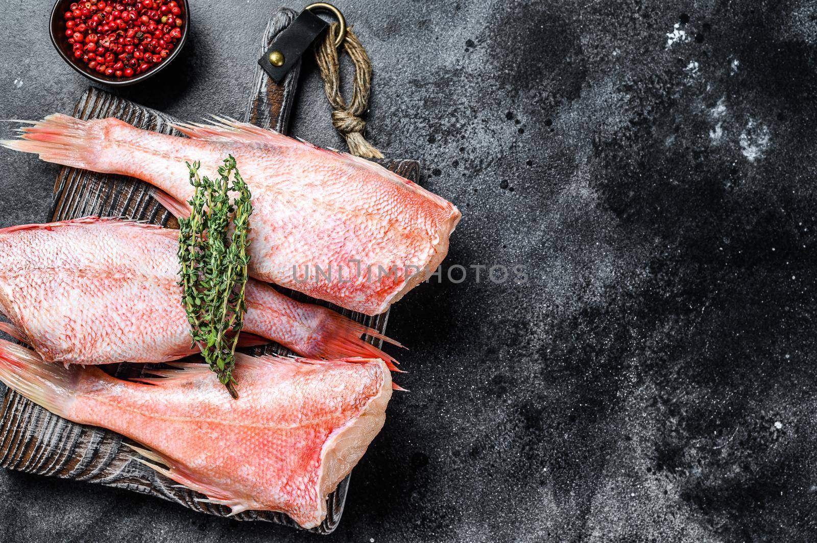 Whole raw red snapper fish on a cutting board. Black background. Top view. Copy space.