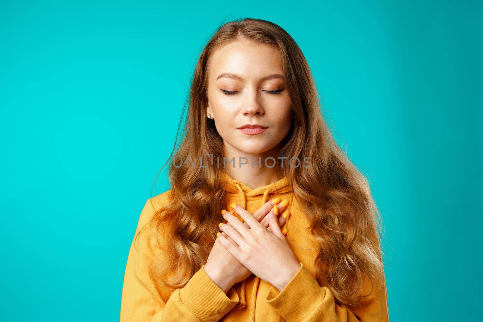 Young casual woman holding hands on her chest and eyes closed, meditating