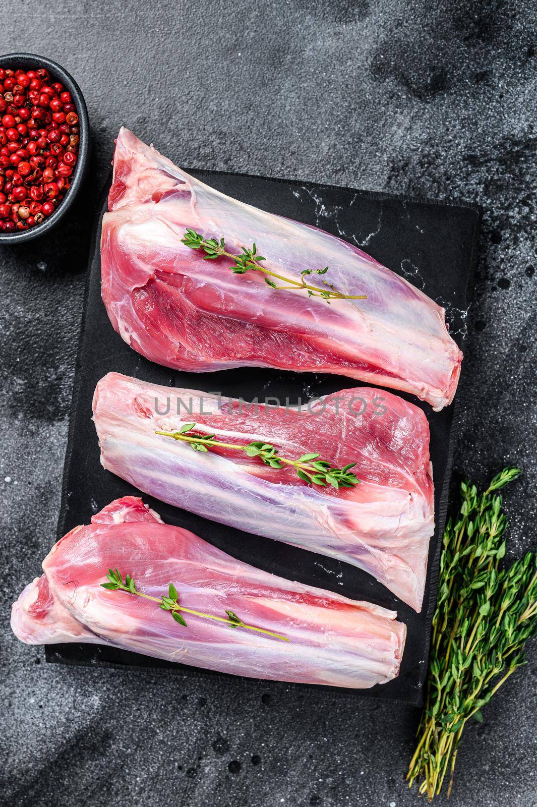 Raw lamb shanks meat on a marble board. Black background. Top view by Composter
