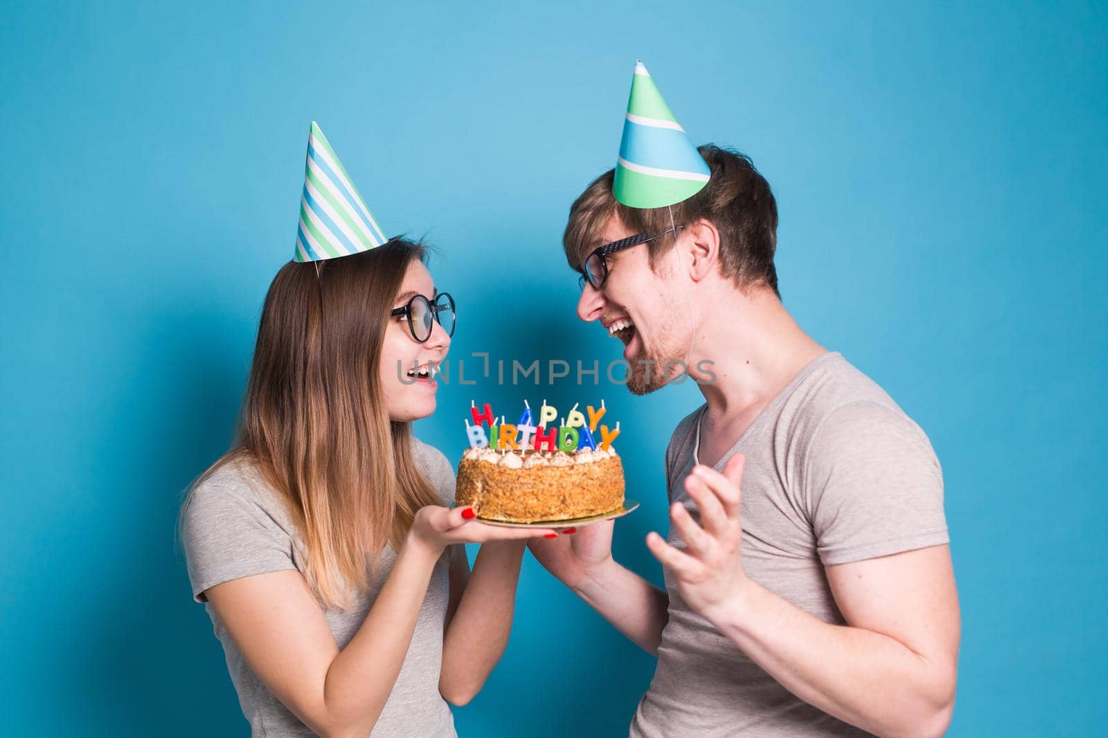 Young cheerful students charming girl and nice guy in greeting paper caps holding a cake with a bengal sparks candle. Concept of congratulations on the holiday and anniversary